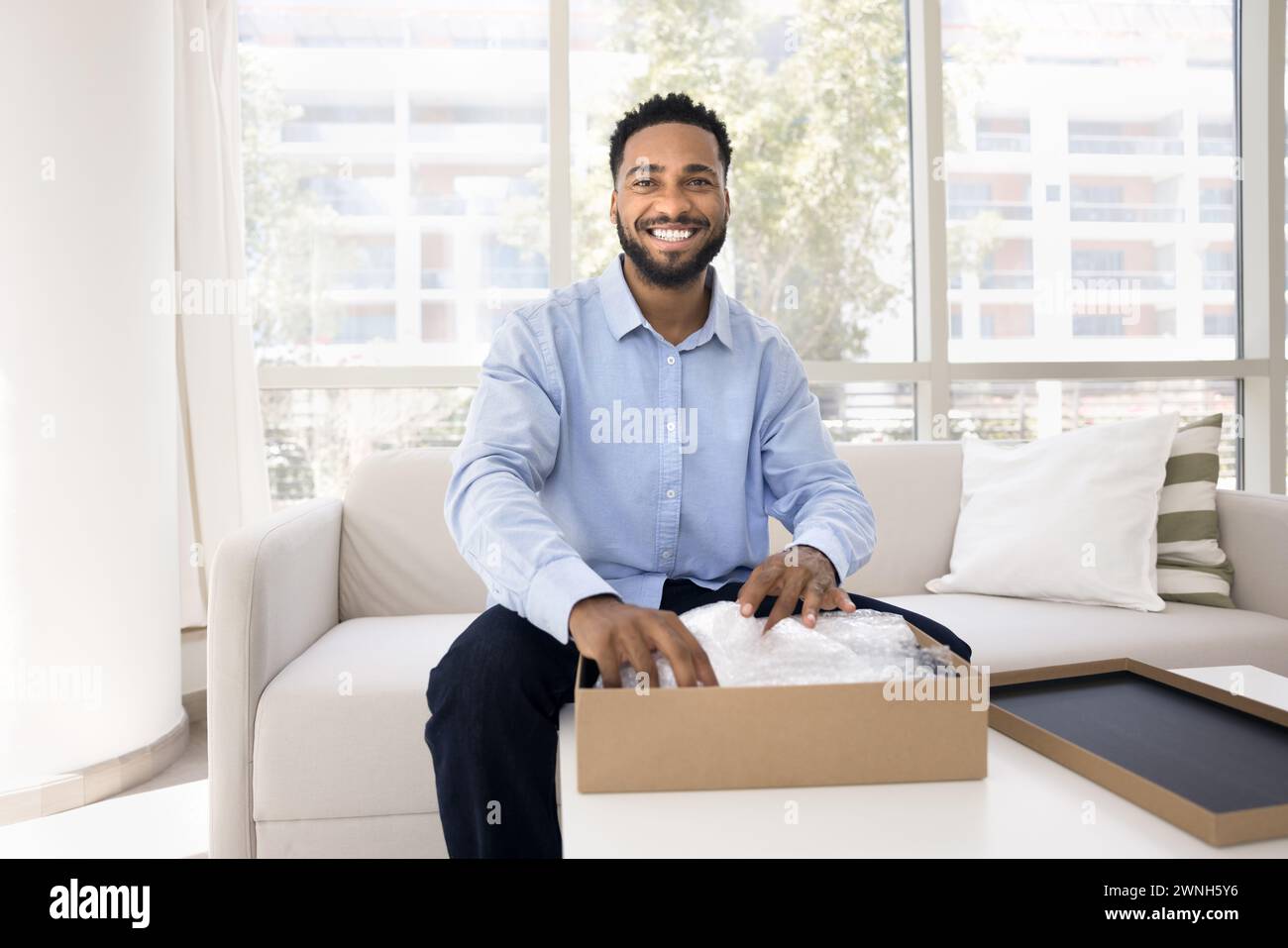 Glücklicher, gutaussehender junger Schwarzer Influencer, der das Paket auspackt Stockfoto
