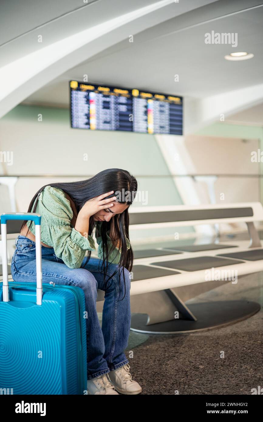 Vertikales Portrait verzweifeltes und gestresstes lateinmädchen am Flughafen, das auf der Bank sitzt und ihre Koffer weint Stockfoto