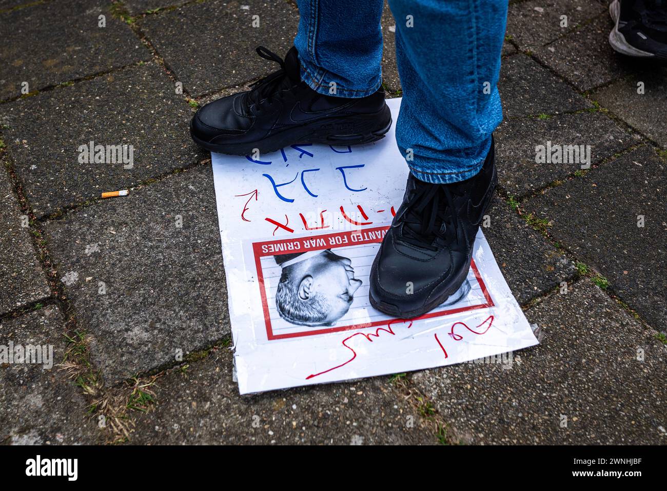 Den Haag, Südholland, Niederlande. März 2024. Ein Demonstrant steht auf einem Fahndungsfoto von BENJAMIN NETANJAHU. Am 2. März 2024 versammelten sich Dutzende pro-palästinensischer Demonstranten in der israelischen Botschaft in den Haag. Ursprünglich als marsch zum niederländischen Repräsentantenhaus geplant, beschränkte der Bürgermeister von den Haag die Demonstration auf einen Park in der Nähe der Botschaft. (Kreditbild: © James Petermeier/ZUMA Press Wire) NUR REDAKTIONELLE VERWENDUNG! Nicht für kommerzielle ZWECKE! Quelle: ZUMA Press, Inc./Alamy Live News Stockfoto