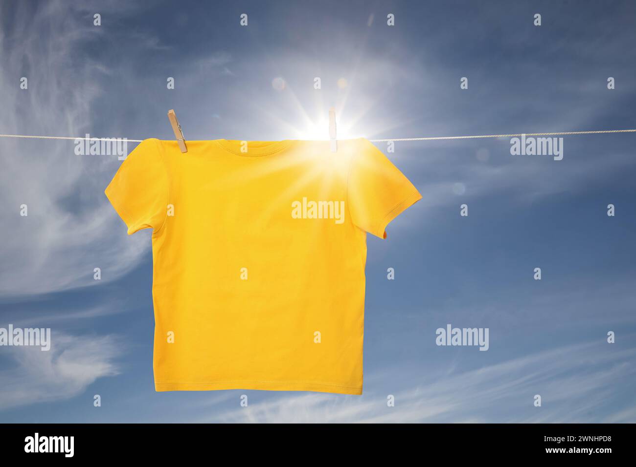 Gelbes T-Shirt, das auf der Wäscheleine vor blauem Himmel trocknet Stockfoto