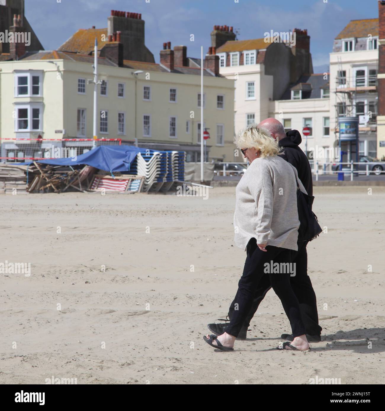 Ein älteres Paar, das am Sandstrand in Weymouth, Dorset, England, Großbritannien spaziert. Stockfoto