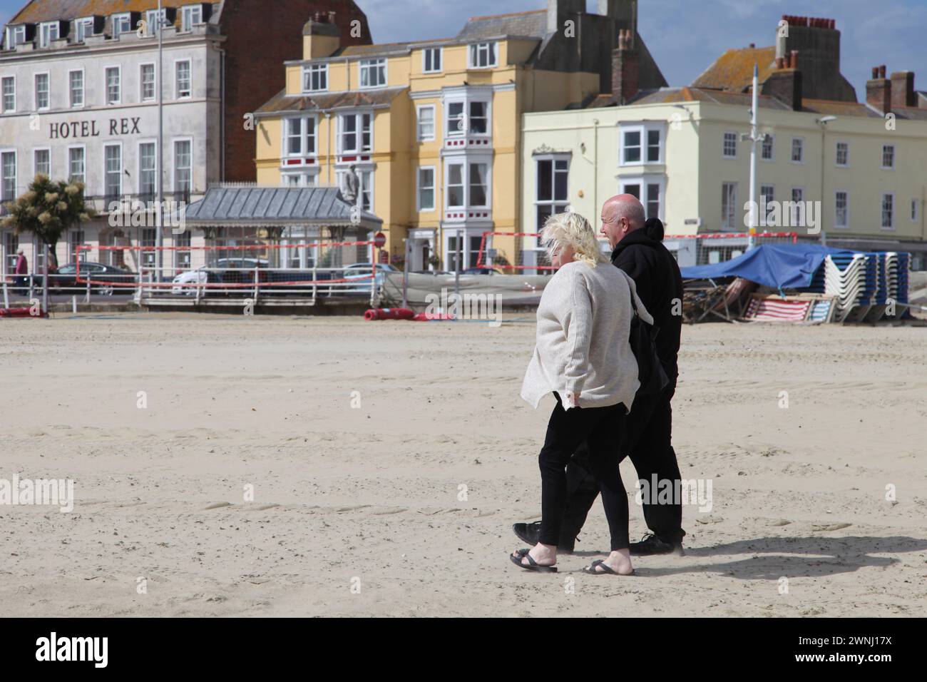 Ein älteres Paar, das am Sandstrand in Weymouth, Dorset, England, Großbritannien spaziert. Stockfoto