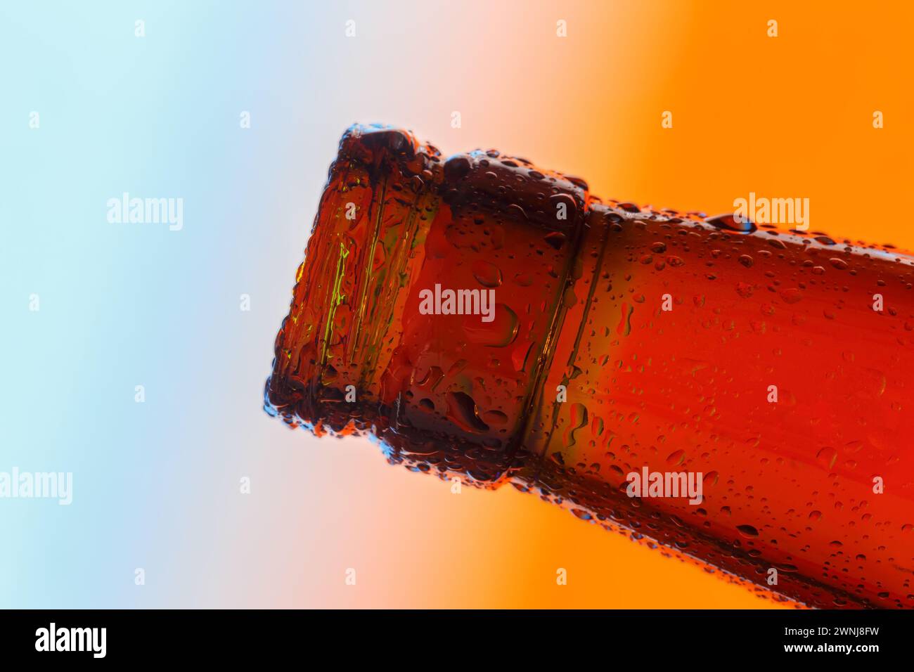 Der Hals einer transparenten Glasflasche ist mit großen Tropfen bedeckt. Nahaufnahme auf einem verlaufenen Hintergrund. Stockfoto