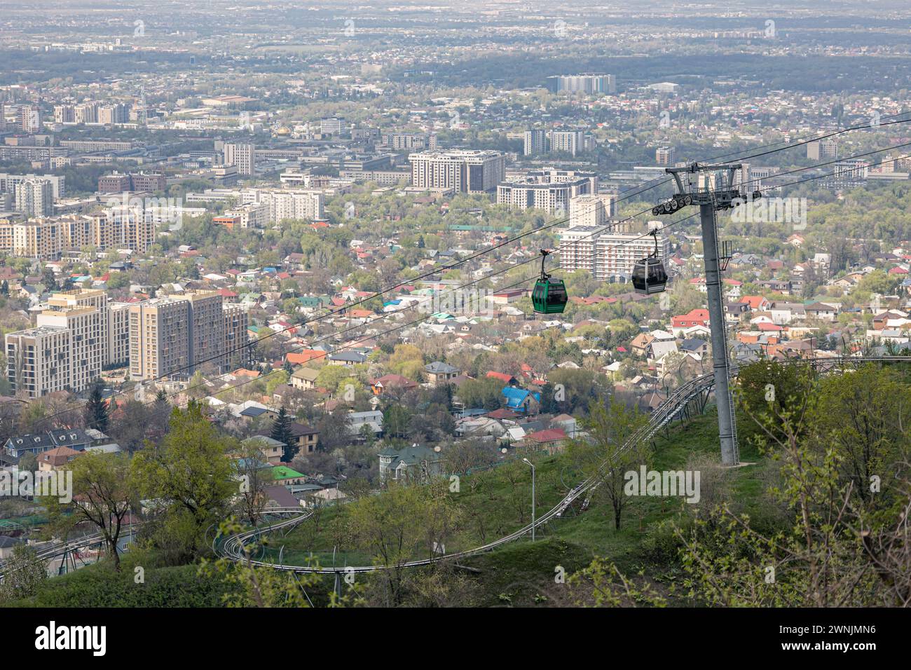 Luftbrücke zum Kok Tobe Hügel in Kasachstan. Seilbahn mit zwei Kabinen, vor dem Hintergrund der Stadt Almaty im Frühling. Touristenort, Stadt Landmar Stockfoto