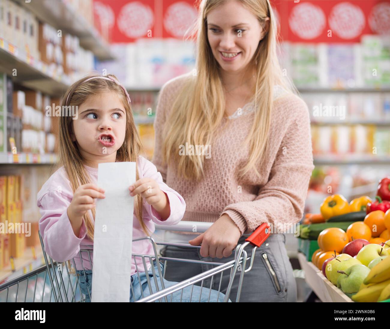 Enttäuschtes Mädchen im Supermarkt mit ihrer Mutter, sie hat eine lange teure Lebensmittelquittung Stockfoto