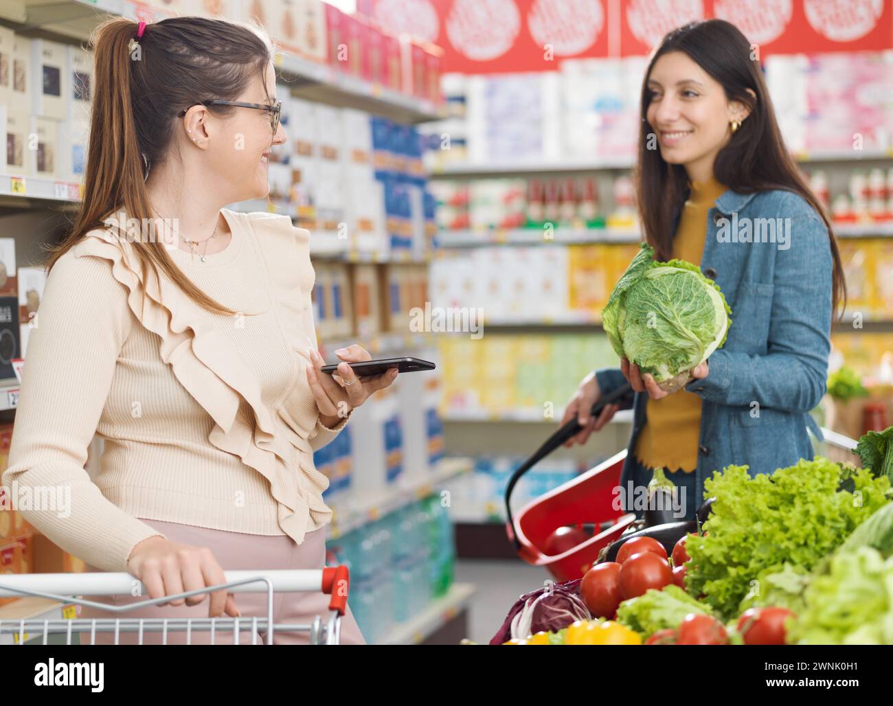 Glückliche Frauen treffen sich im Supermarkt, sie reden und kaufen zusammen frisches gesundes Gemüse, Lebensmittelgeschäft und Lifestyle Konzept Stockfoto
