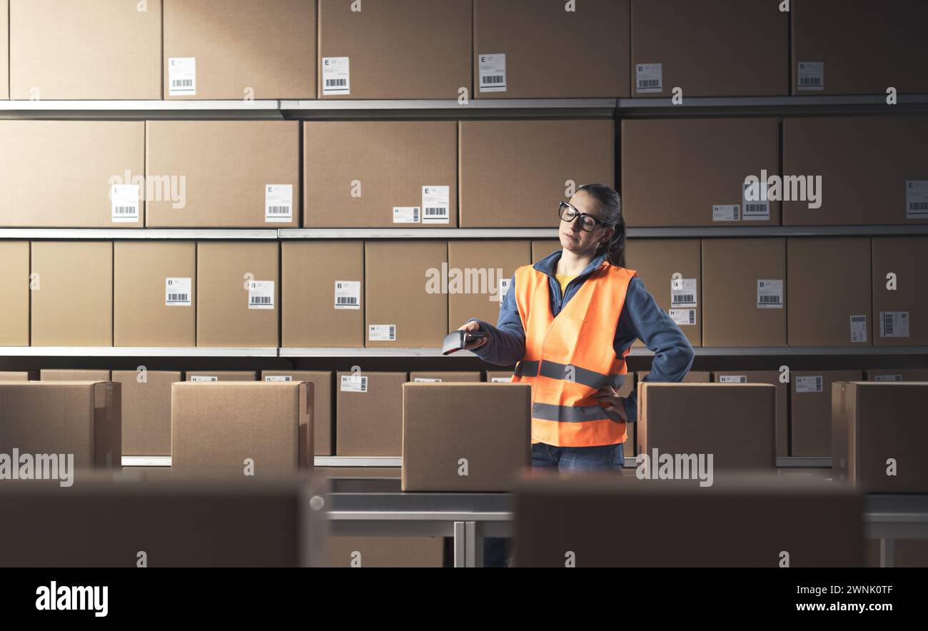 Die langweilige Frau, die im Lagerhaus arbeitet, scannt Barcodes auf Kisten mit einem Scanner Stockfoto