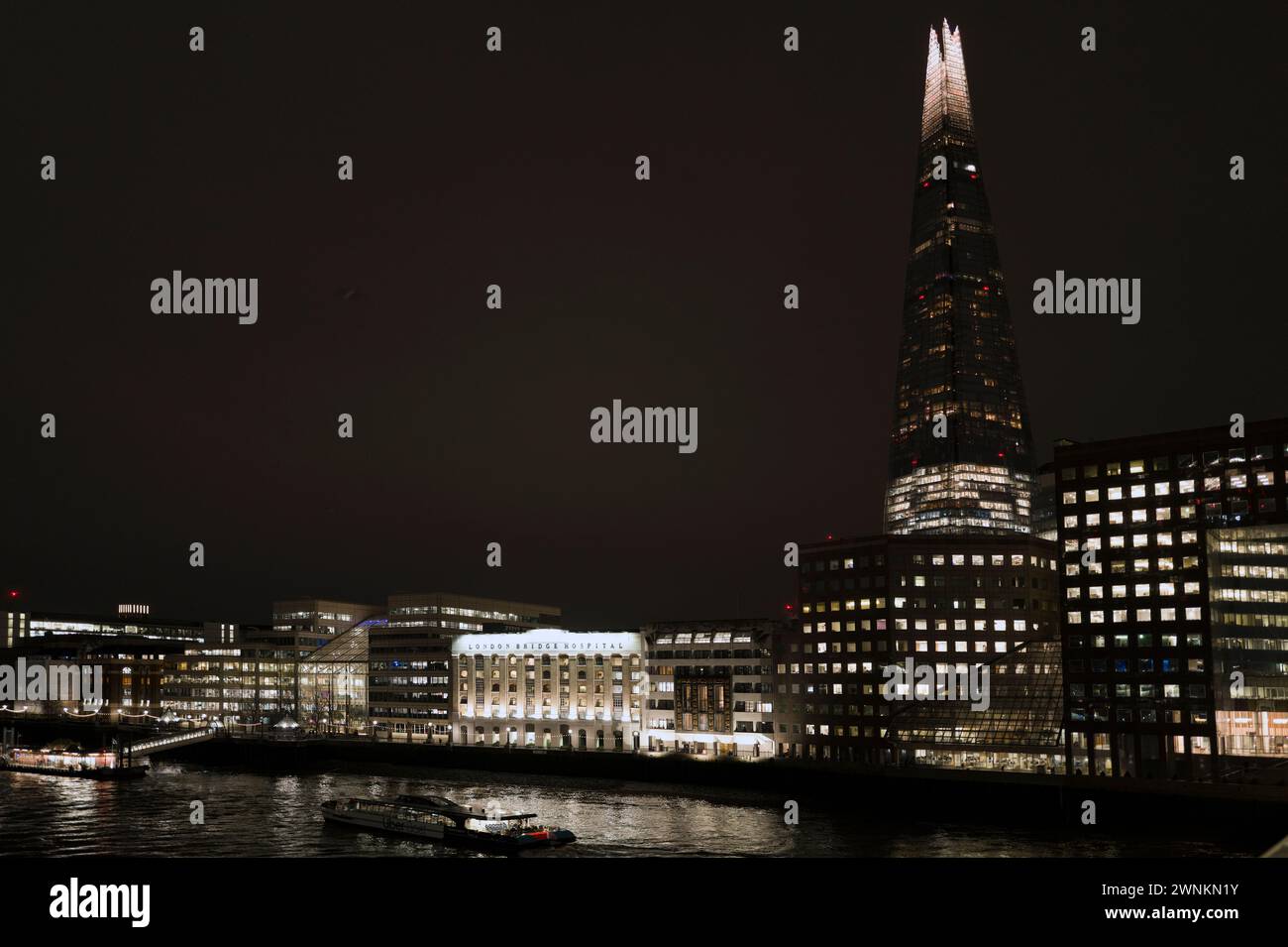 Kraftvolle abstrakte, architektonisch beleuchtete Nachtlandschaft der Shard und der Themse, aufgenommen von der London Bridge und zeigt Tooley Street, London Bridge Hospital, HMS Belfast, London Bridge City Pier und River Boats Stockfoto