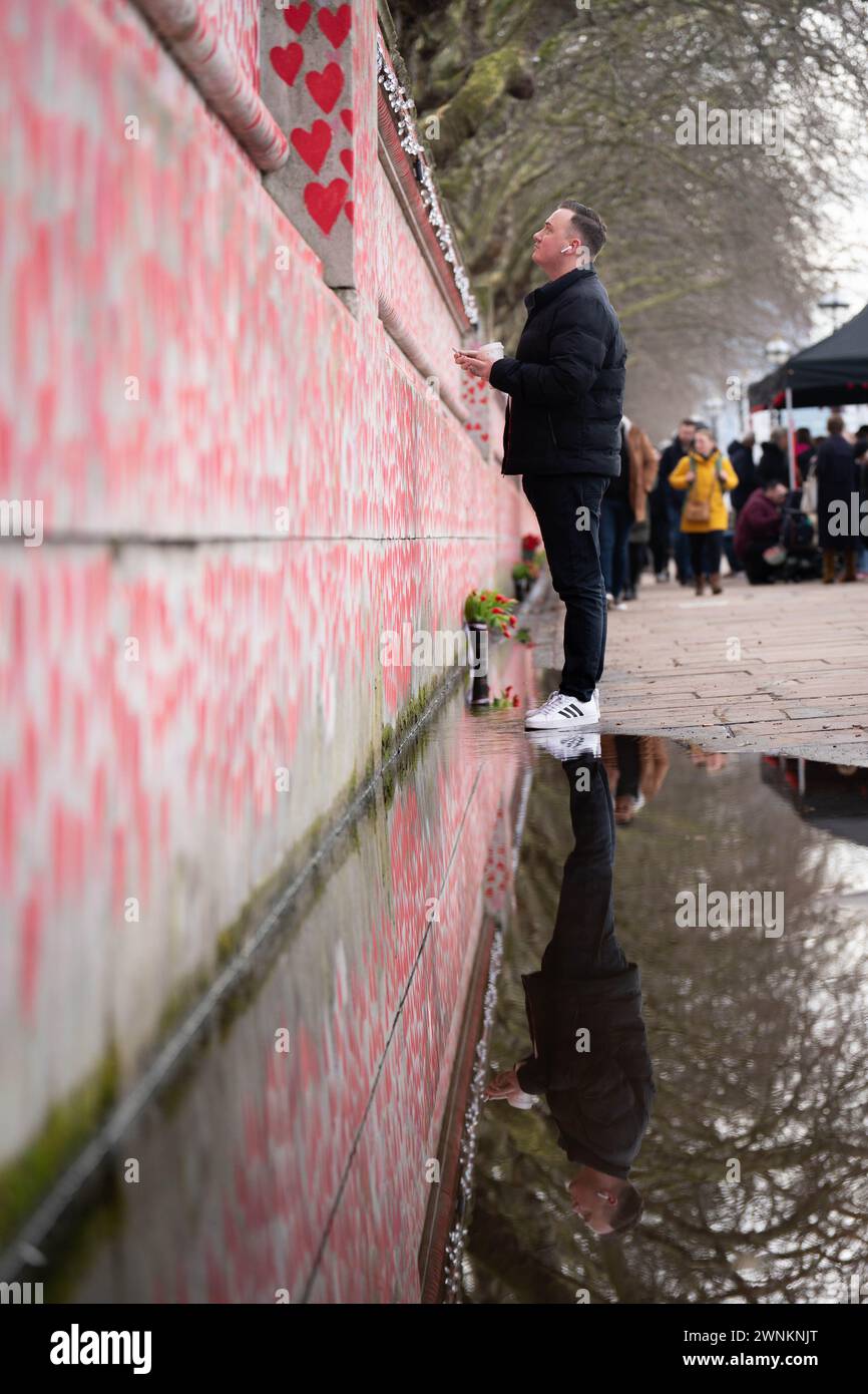 Die Menschen schreiben Namen auf die COVID Memorial Wall am Themsepfad in Westminster, um Reden und eine Schweigeminute am Nationalfeiertag der Reflexion zu Ehren derer zu halten, die an COVID-19 gestorben sind. Jedes handgemalte Herz an der Wand repräsentiert ein Leben, das in Großbritannien an COVID-19 verloren ging. Bilddatum: Sonntag, 3. März 2024. Stockfoto