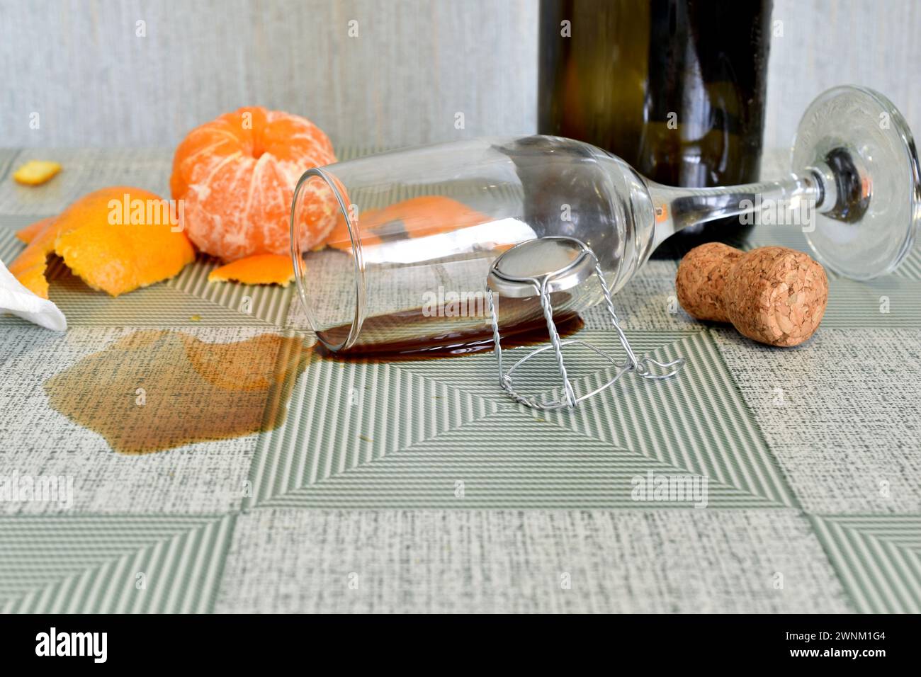Das Glas liegt in einer Weinpfütze auf dem Tisch, daneben stehen eine leere Flasche und Obst. Stockfoto