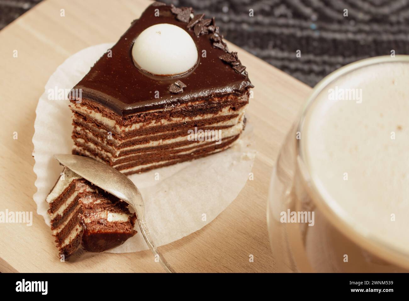 Schokoladenkuchen mit Kaffeetasse. Kekskuchen mit geschmolzener Ganache darauf. Scheibe cremige Tarte und Latte. Dessert mit Vanille und Kakaoschicht. Stockfoto