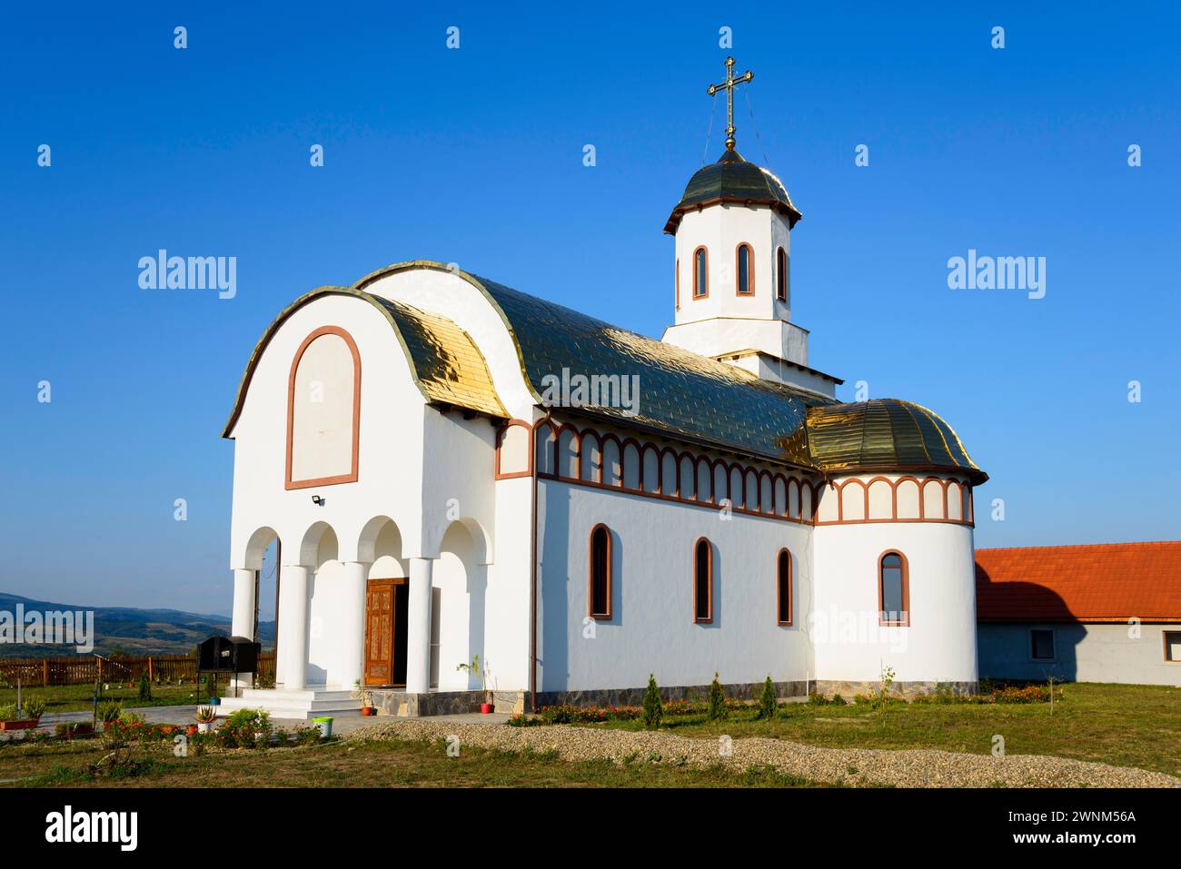 Eine kleine Kirche mit einer weiß-goldenen Fassade unter einem blauen Himmel sieht friedlich und einladend aus, Tara Almajului Nonnenkloster, im Zentrum des Stockfoto