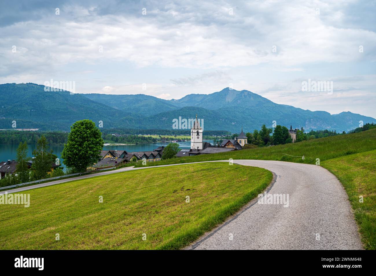 Ein malerischer Weg führt zu einer Kirche mit Blick auf einen See und die umliegenden Hügel, Sankt Wolfgang, Wolfgangsee, Salzkammergut, Österreich Stockfoto