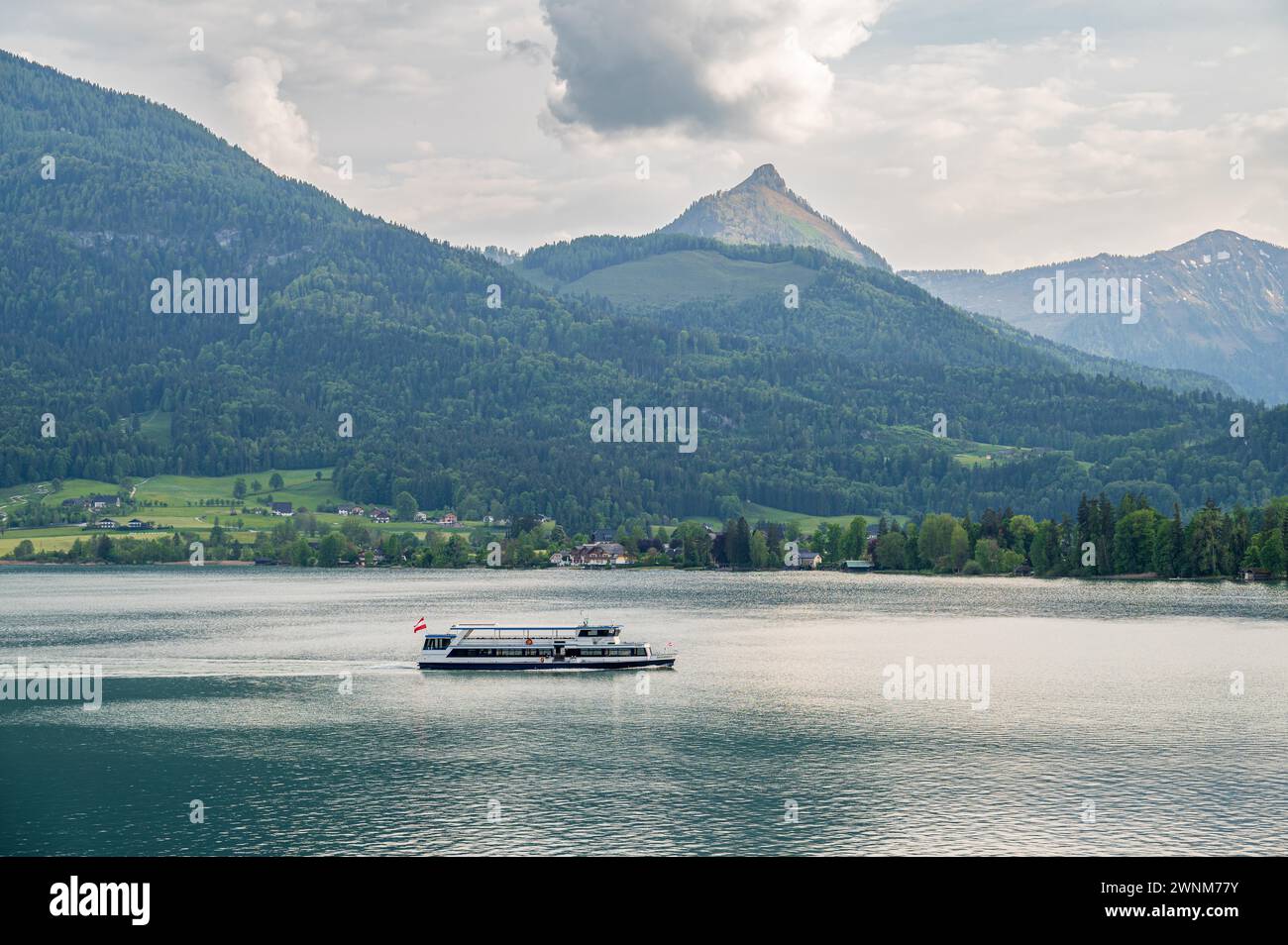 Boot gleitet ruhig über einen See mit einem Berg im Hintergrund und einem bewölkten Himmel, Wolfgangsee, Salzkammergut, Österreich Stockfoto
