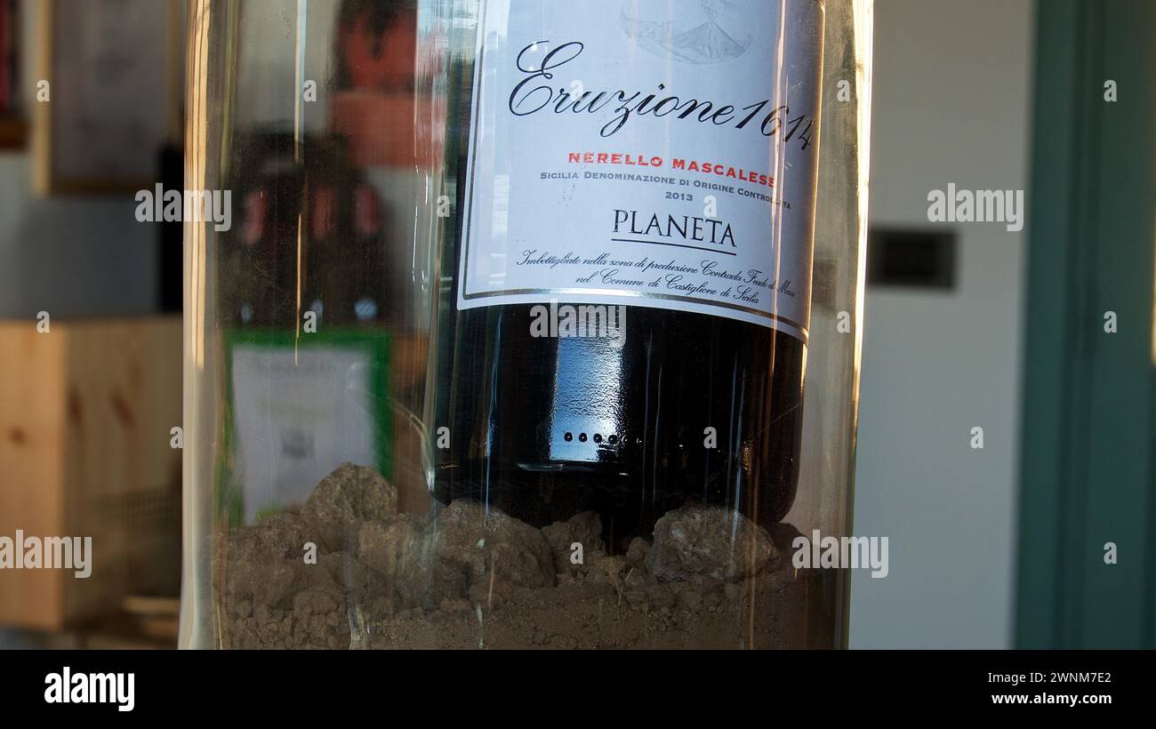 Weinflasche in einem Glasbehälter, präsentiert auf Sand, Schwerpunkt auf Etikett, Weingut Planeta, sizilianischer Wein, Sizilien, Italien Stockfoto
