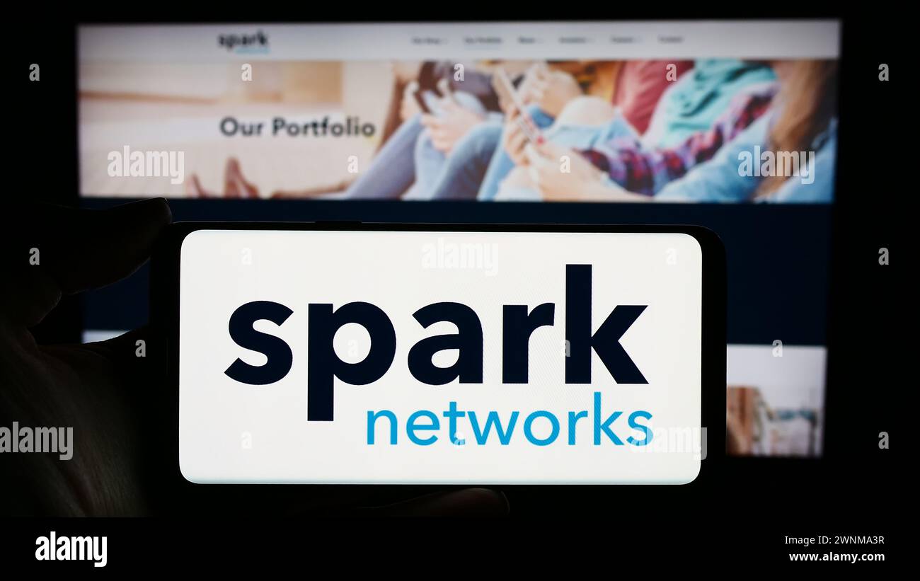 Person mit Handy mit Logo der Online-Dating-Firma Spark Networks SE vor der Business-Website. Schwerpunkt auf dem Display des Telefons. Stockfoto