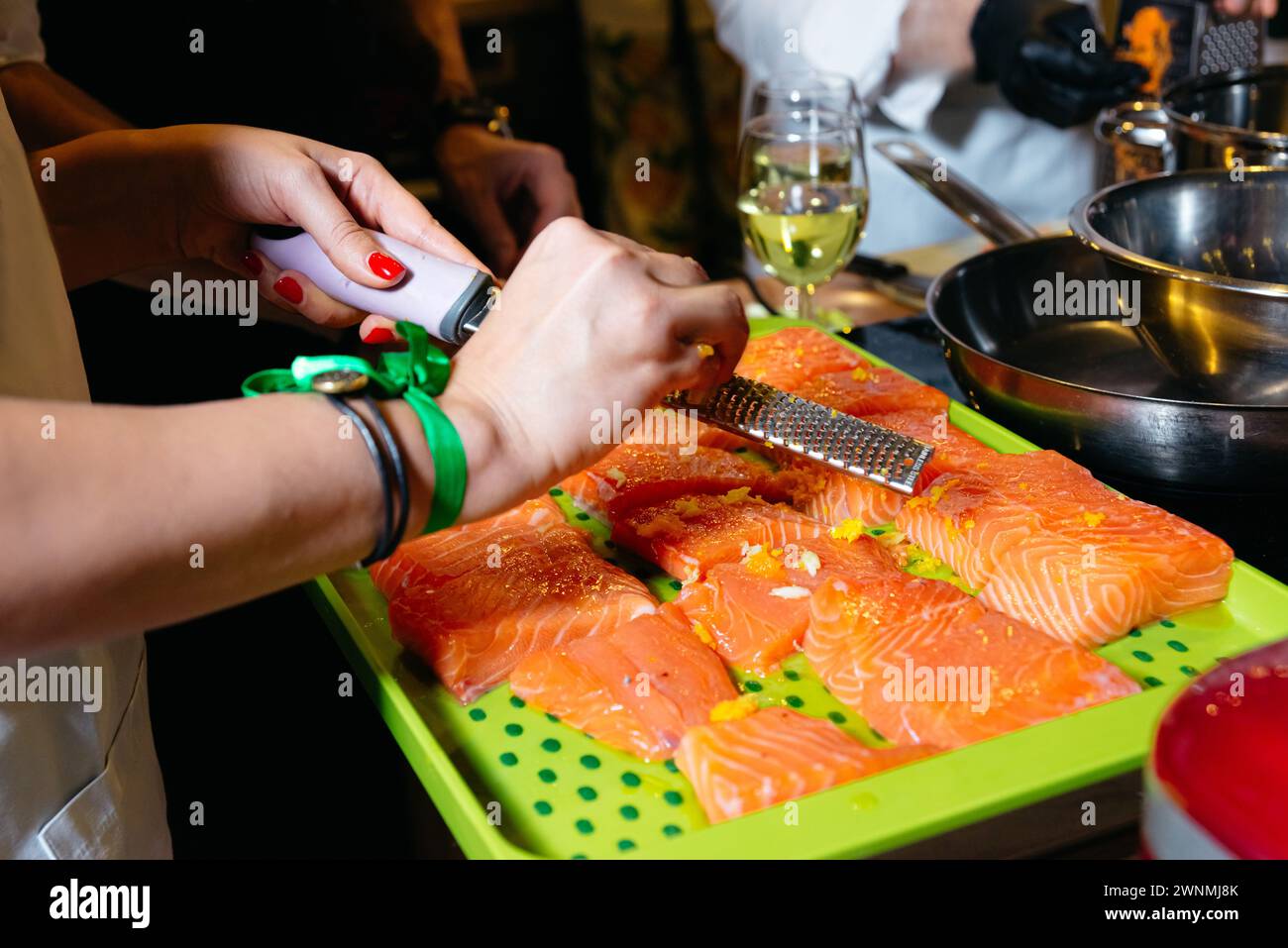 Ein Küchenchef zerkleinert vorsichtig Zitrone auf frische Lachsfilets und fügt den Meeresfrüchten vor dem Kochen einen Hauch Zitrusgeschmack hinzu. Stockfoto