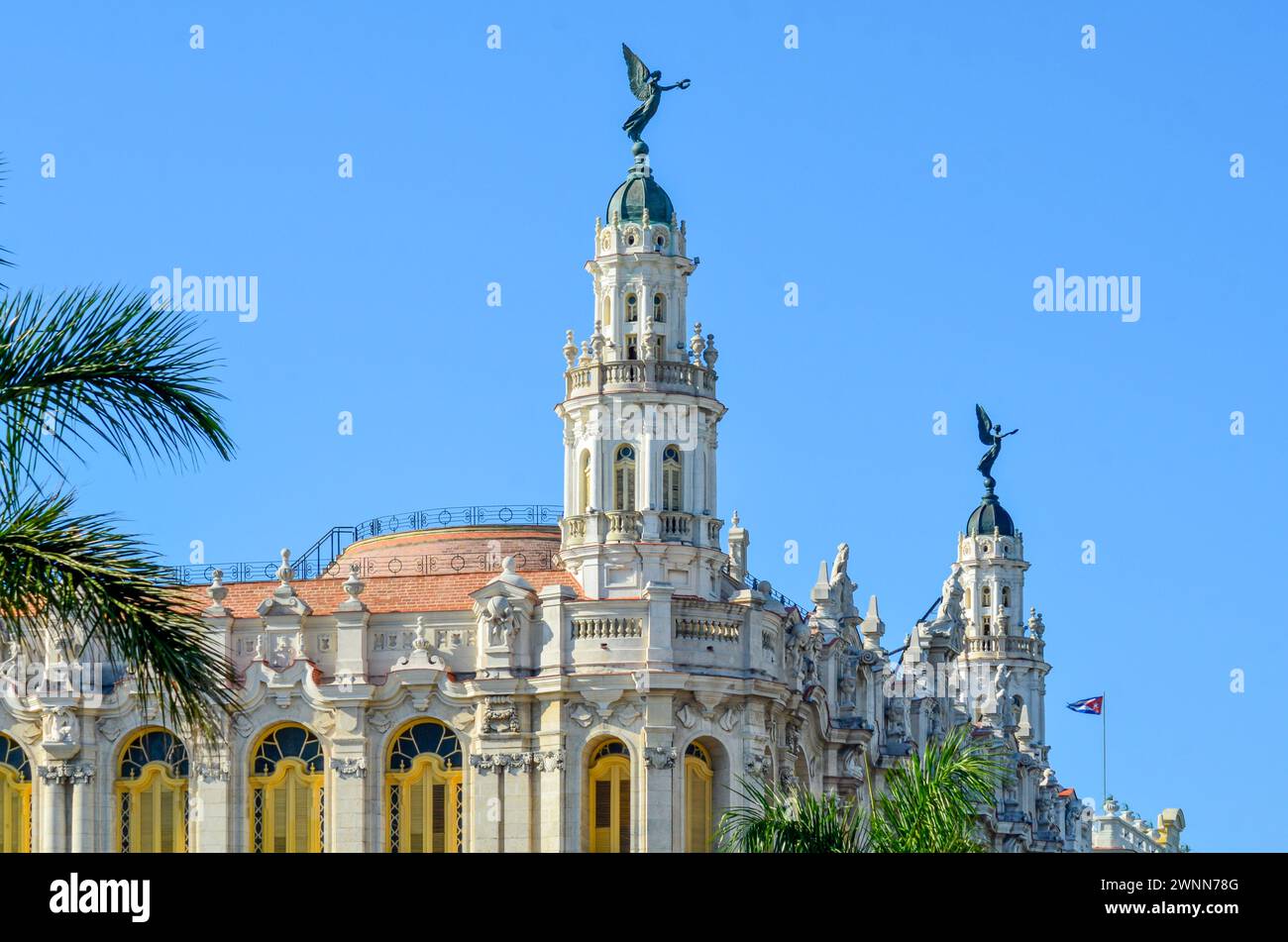 Großes Theater von Havanna, 2 Türme, 2 Engelsstatuen, Kuba Flagge, hellgelbe Fensterläden, Marmorstein, grüne Palmen, blauer Himmel. Stockfoto