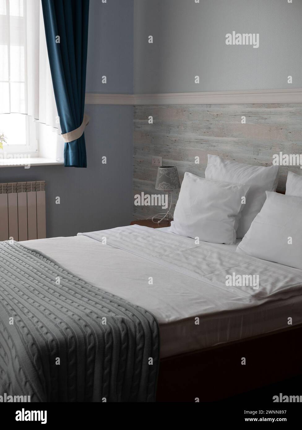 Ordentlich gemachtes Bett in einem modernen und gemütlichen Hotel- oder Apartmentzimmer, selektiver Fokus. Minimaler und komfortabler Schlafbereich, aufrechtes Format Stockfoto