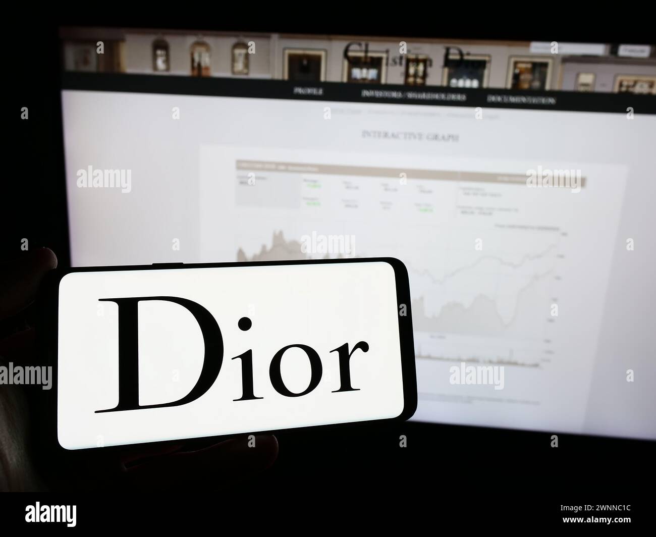 Person, die ein Mobiltelefon mit dem Logo des französischen Luxusmodeunternehmens Christian Dior SE vor der Business-Webseite hält. Schwerpunkt auf dem Display des Telefons. Stockfoto