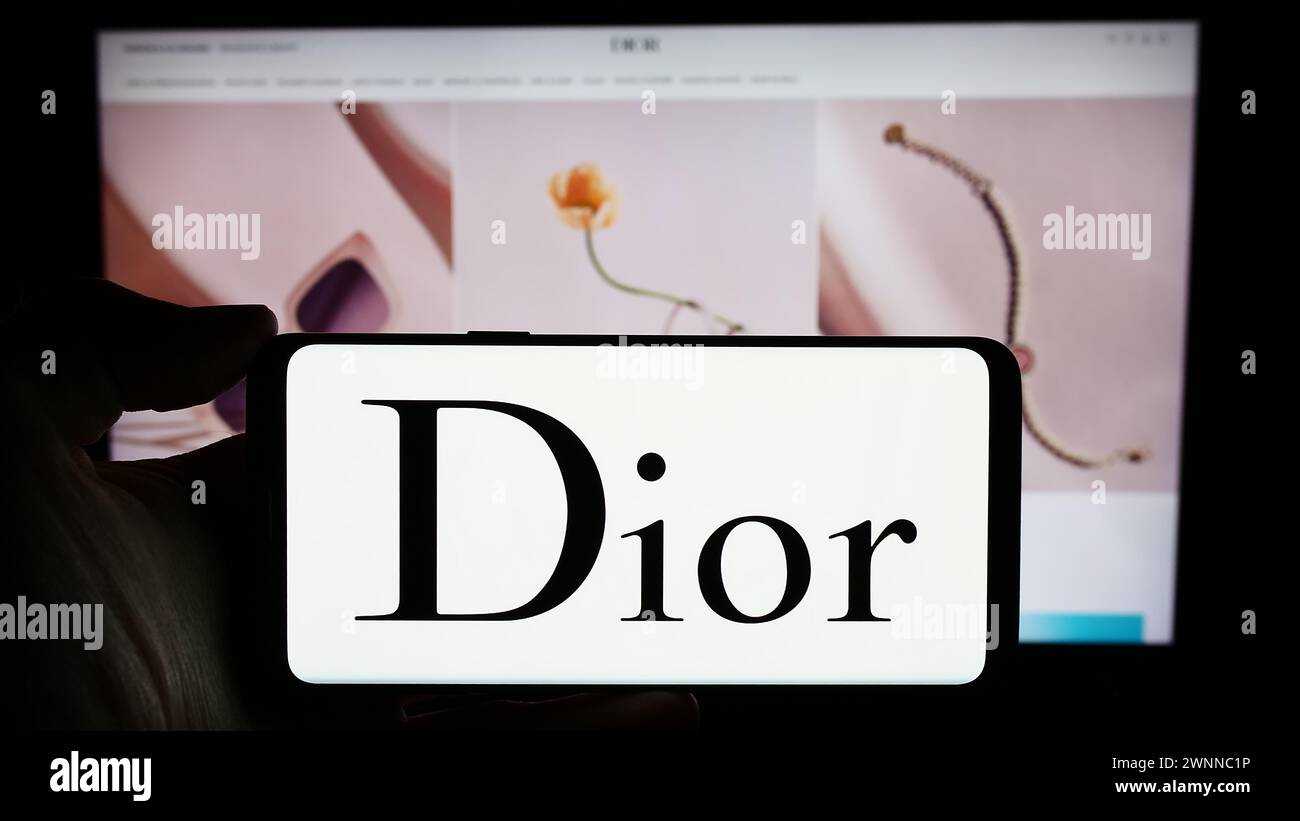 Person mit Smartphone und Logo des französischen Luxusmodeunternehmens Christian Dior SE vor der Website. Schwerpunkt auf dem Display des Telefons. Stockfoto