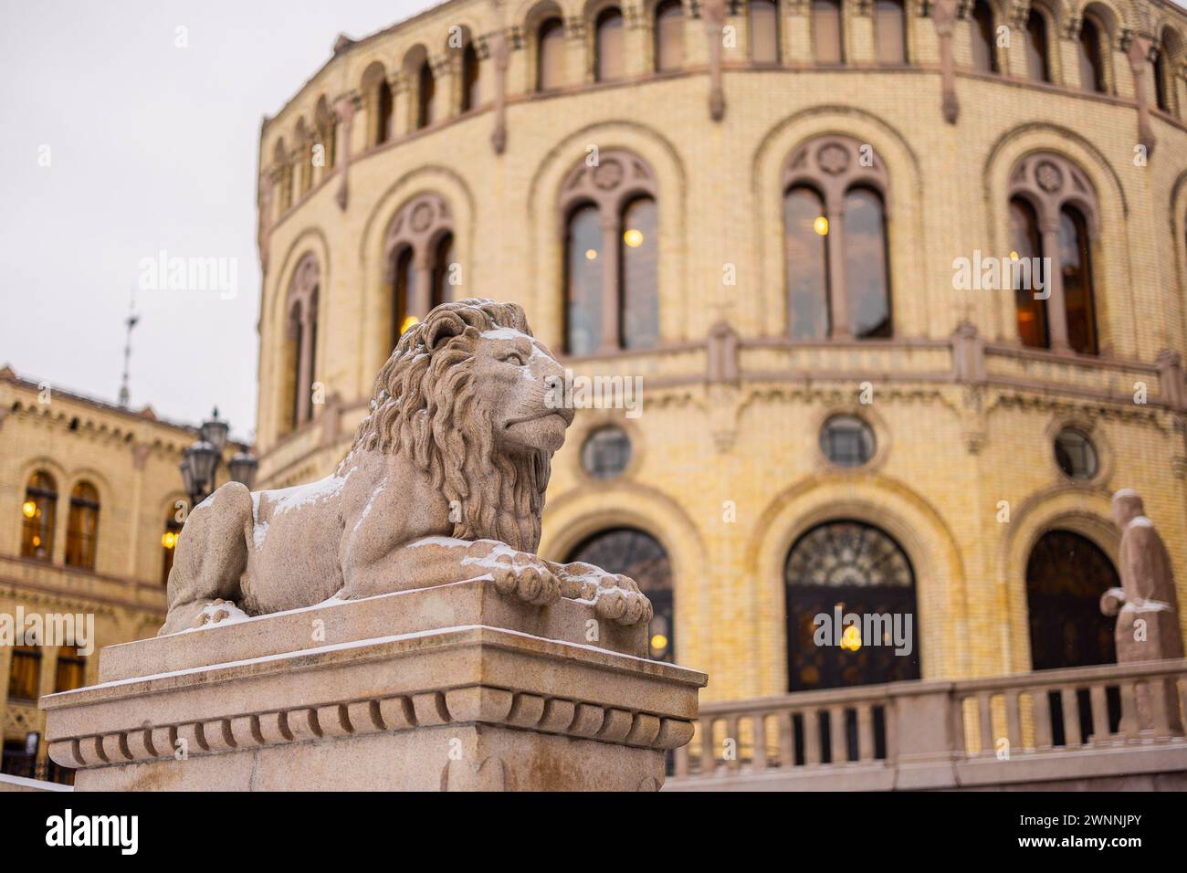 Statue eines Löwen vor dem Haus des norwegischen parlaments an einem kalten Wintertag. Der Löwe ruht friedlich auf einer Säule vor dem majestätischen Gebäude Stockfoto