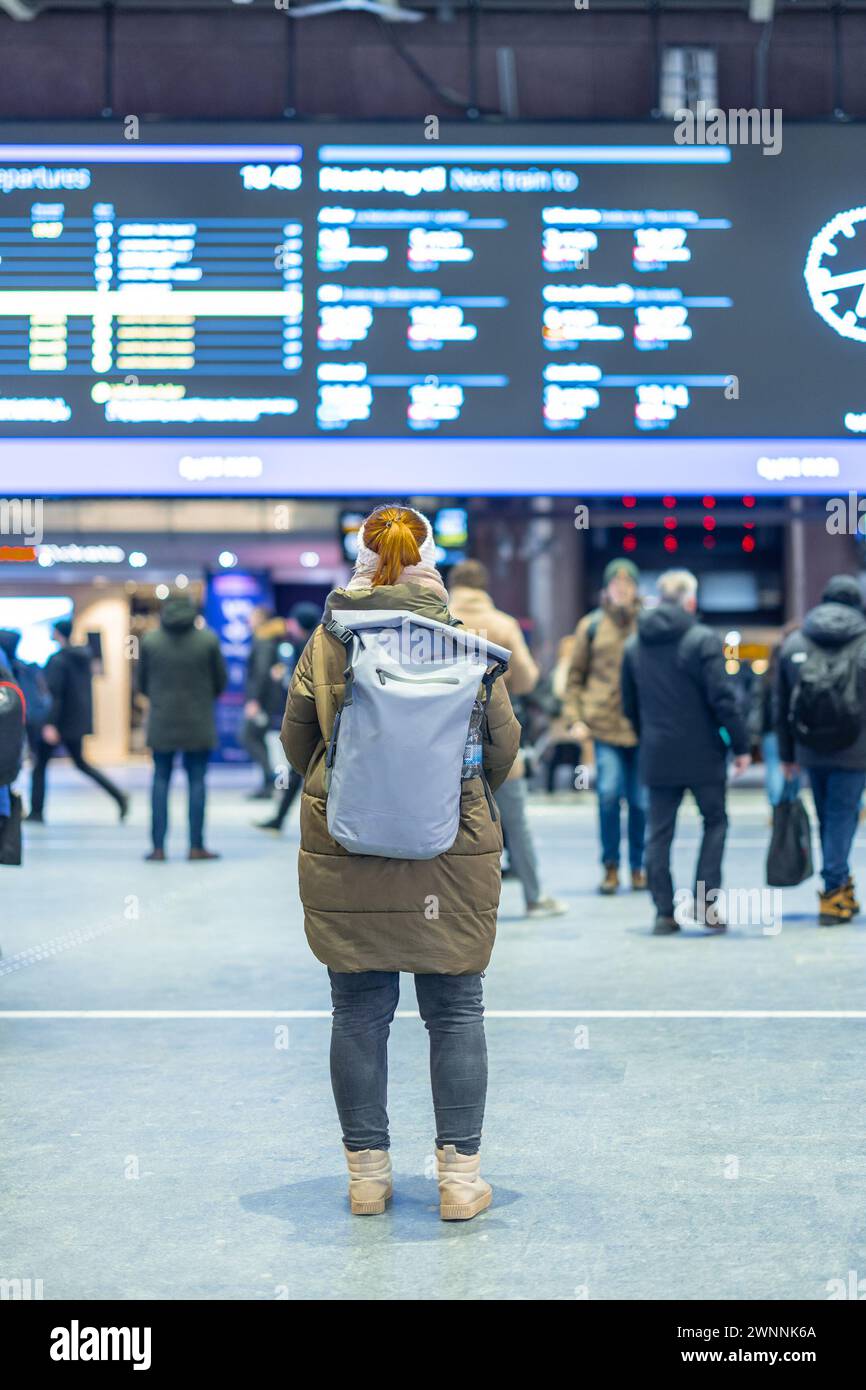 Rückansicht einer unbekannten Frau in orangefarbenem Haar in der Abfahrtshalle am S-Bahnhof Oslo, mit einer grauen Tasche auf der Tasche. Glücklicher Reisender in oslo. Stockfoto