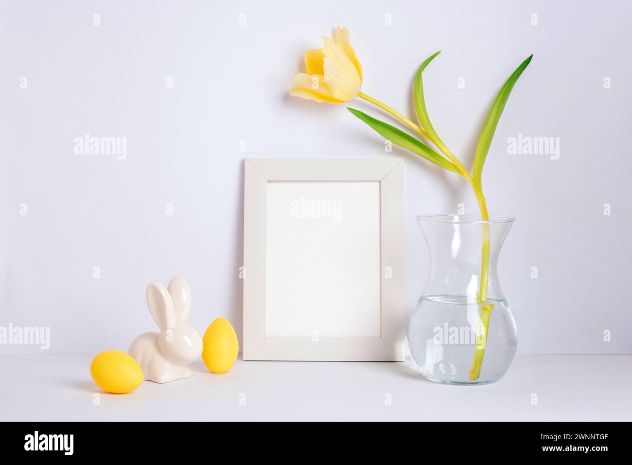 Leerer Bilderrahmen, gelbe Tulpe in Vase und Osterdekorationen auf weißem Hintergrund. Osterkonzept. Stockfoto