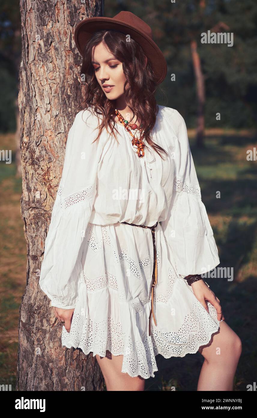 Outdoor-Mode: Porträt des schönen jungen Boho (Hippie) Mädchens im Wald. Niedliche Hippie steht am Baum bei Sonnenuntergang Stockfoto