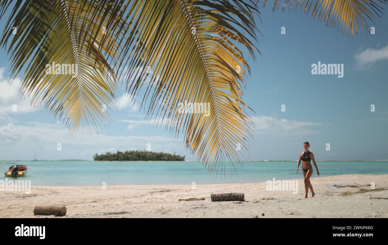 Frau spaziert unter Palmen am tropischen Strand, klarem blauem Himmel und kristallklarem Wasser, kleine Insel. Ruhiges Meer, weißer Sand, friedliche Szene. Weibliche Touristin im Sommerurlaub. Lifestyle-Urlaubskonzept Stockfoto