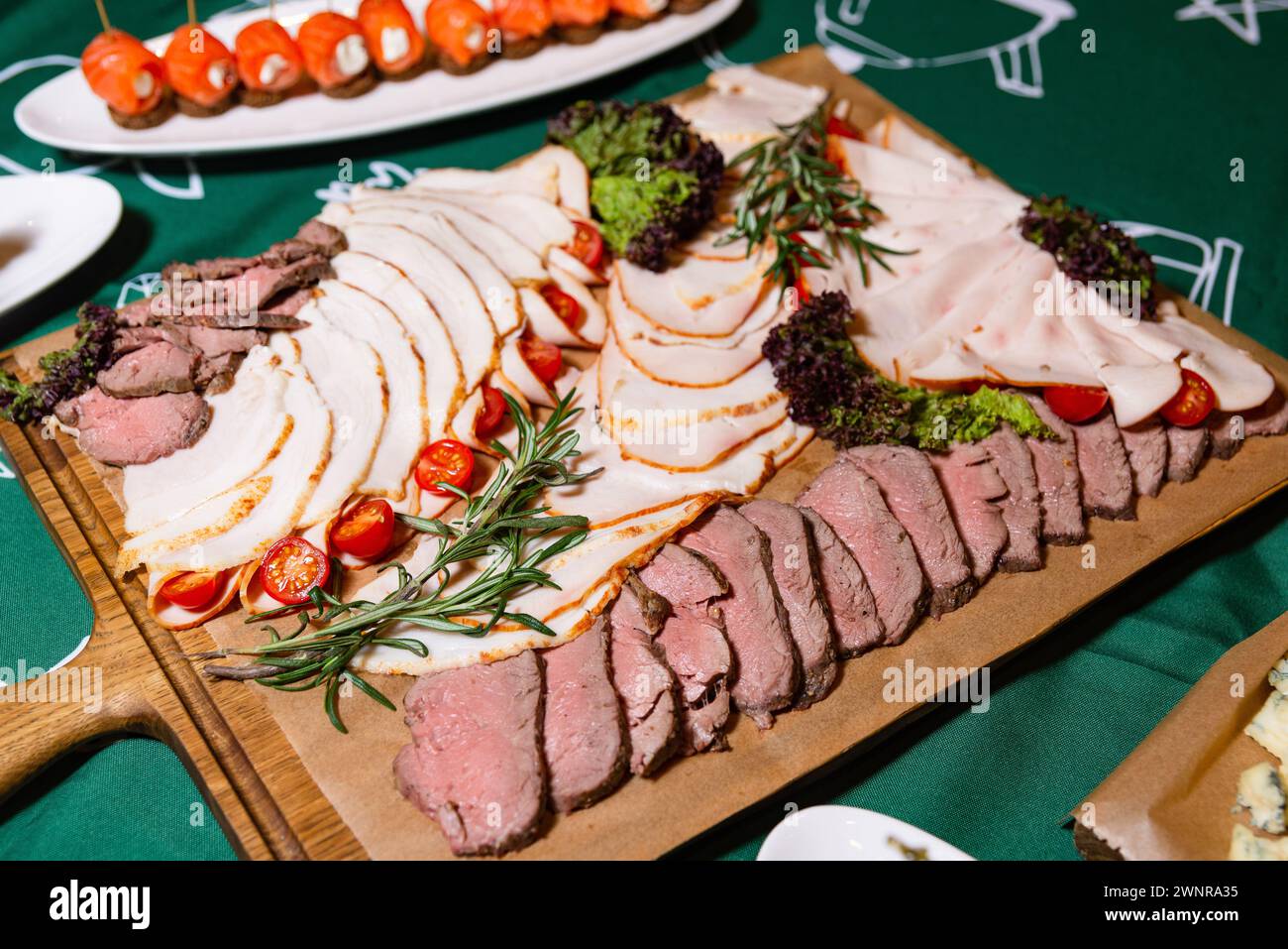 Eine verführerische Platte mit verschiedenen Wurstwaren, einschließlich truthahnscheiben und Roastbeef, garniert mit Kirschtomaten und frischen Kräutern. Stockfoto