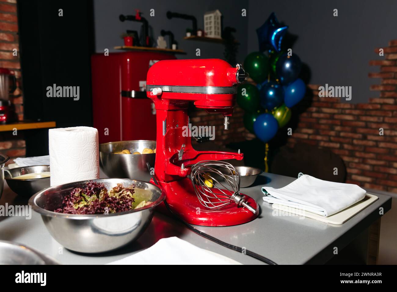 Ein leuchtend roter Standmixer auf einer Küchentheke, mit einer Schüssel Salat und festlichen Ballondekorationen im Hintergrund Stockfoto
