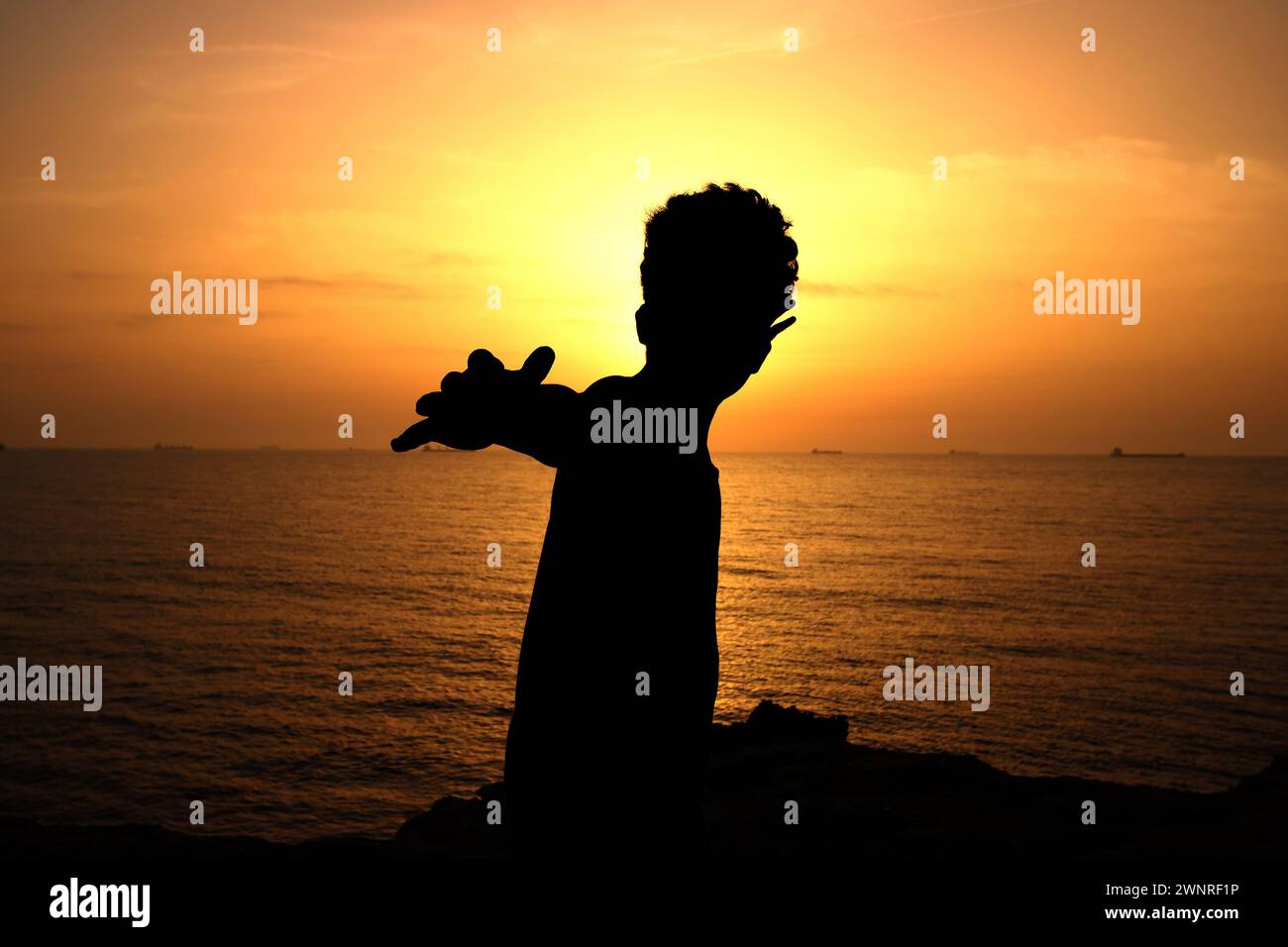 Silhouette von Kinderarmen, die bei Sonnenuntergang mit dem Rücken zum Meer gestreckt sind Stockfoto