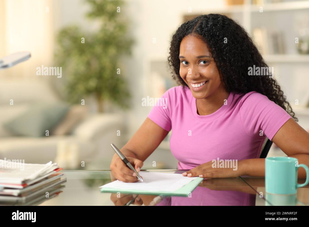 Glückliche schwarze Frau, die einen Vertrag unterschreibt oder ein Formular ausfüllt, sieht dich zu Hause an Stockfoto