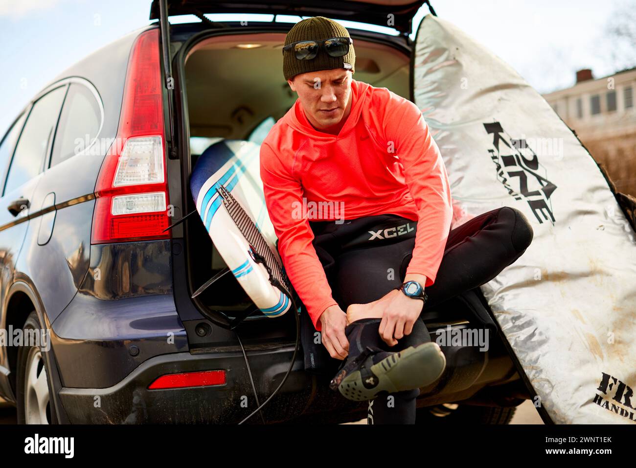 Ein Surfer, der im Kofferraum sitzt und sich auf das Surfen vorbereitet Stockfoto