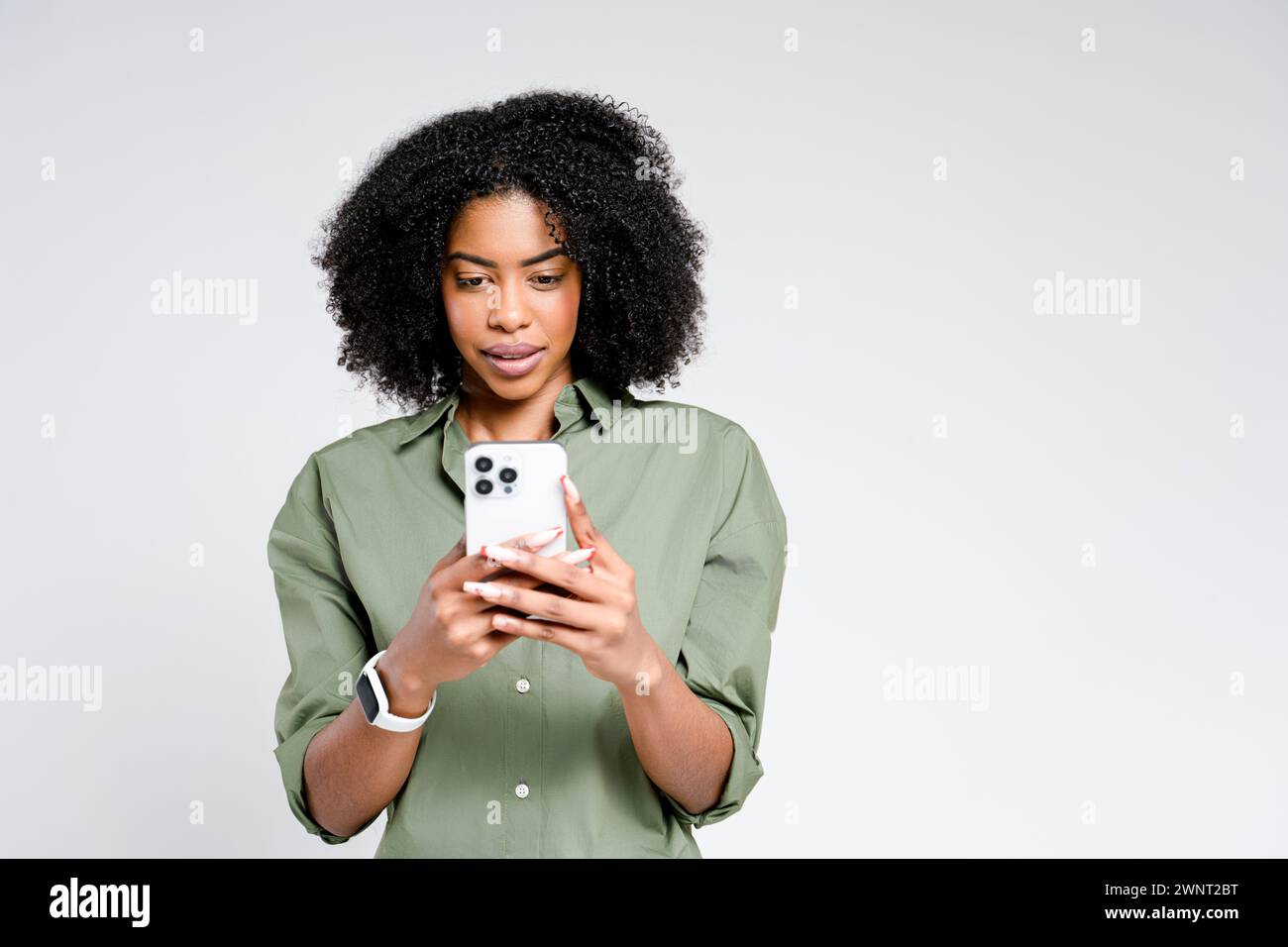 Eine kontemplative afroamerikanische Frau hält ihr Smartphone mit nachdenklichem Ausdruck fest und weist auf einen Moment der Entscheidung oder Reflexion hin. Stockfoto