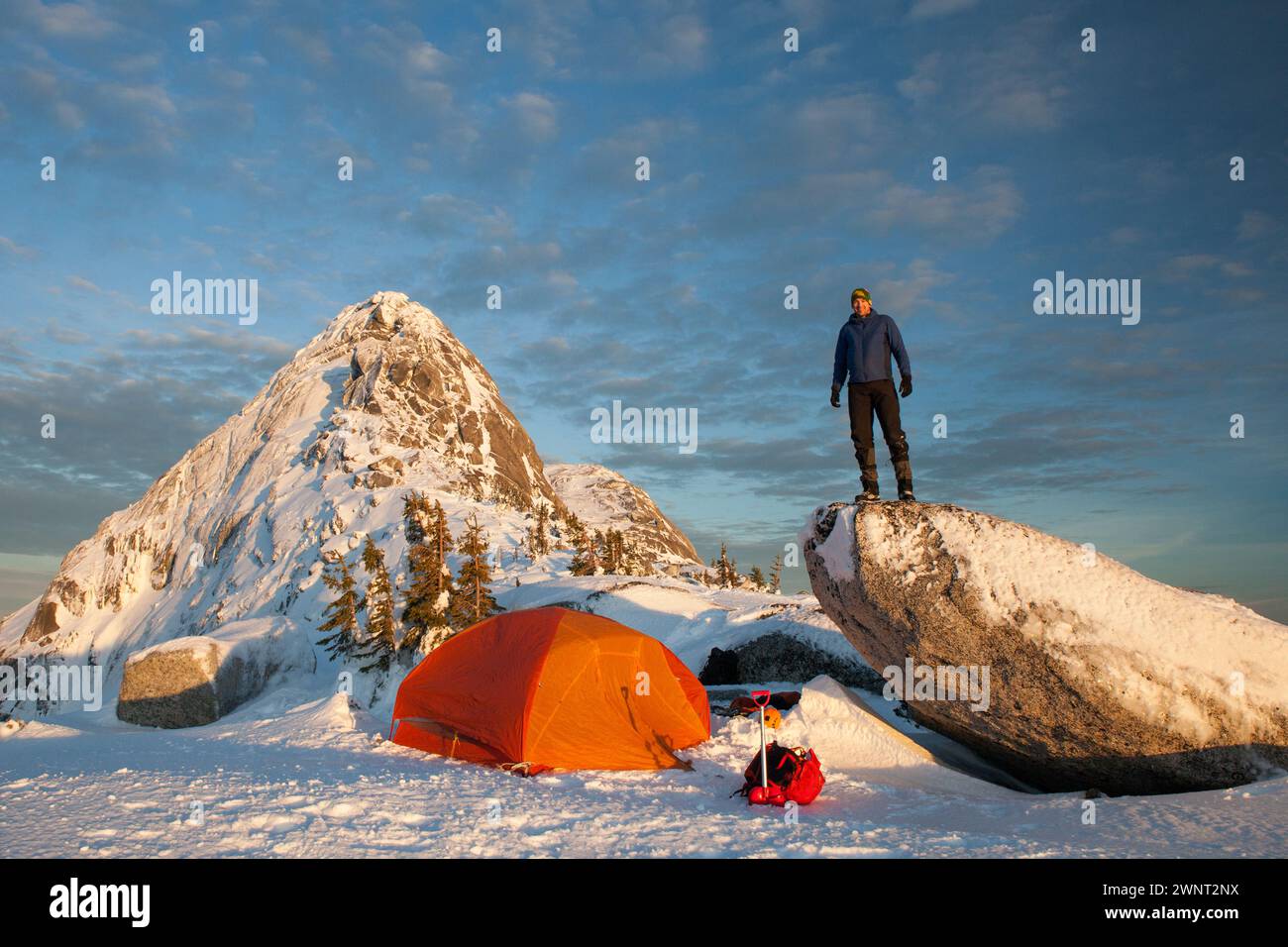 Bergsteiger, der vor dem Zelt unter dem Berggipfel steht Stockfoto