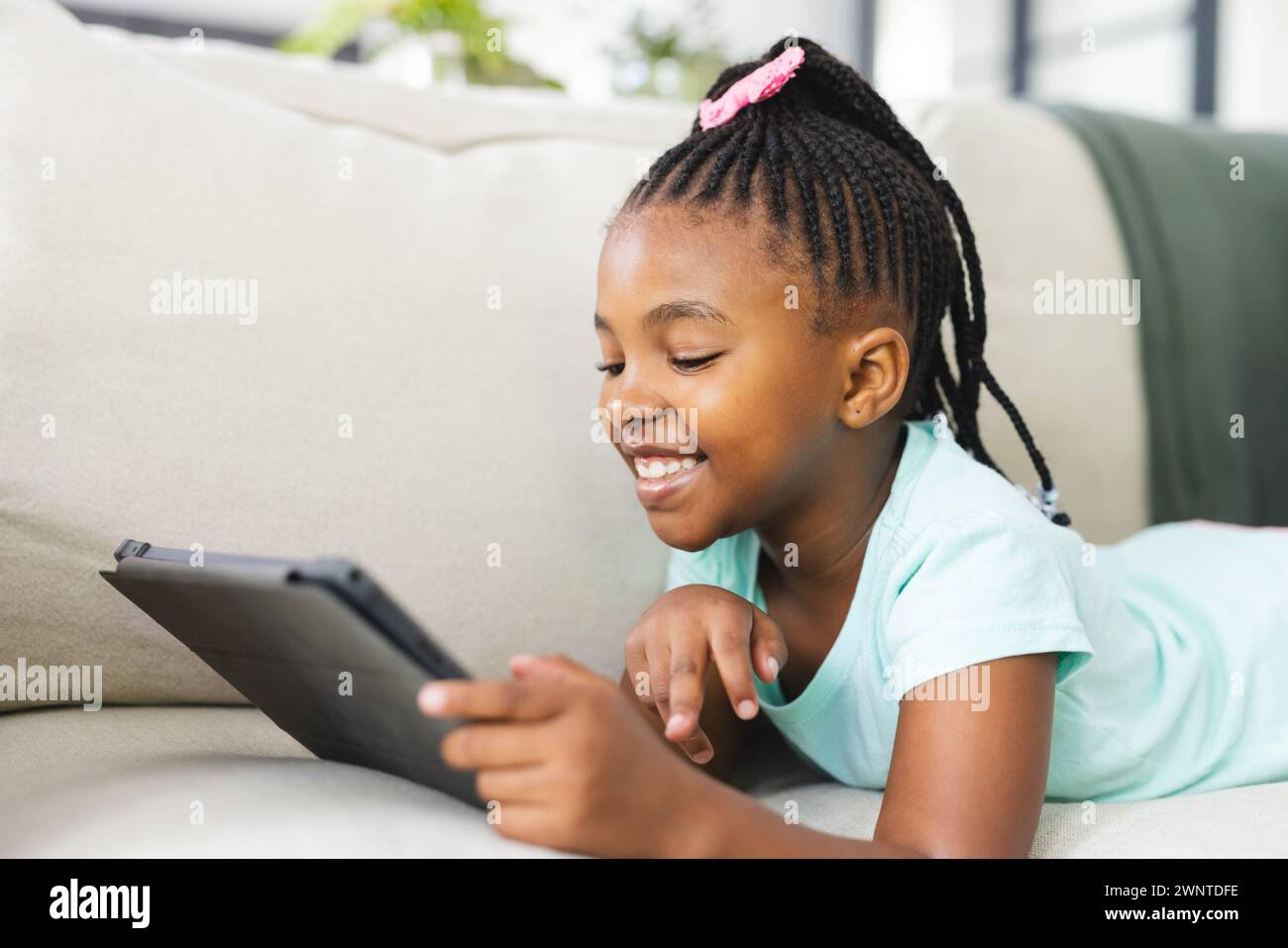 Ein afroamerikanisches Mädchen mit geflochtenen Haaren benutzt eine Tablette auf der Couch Stockfoto