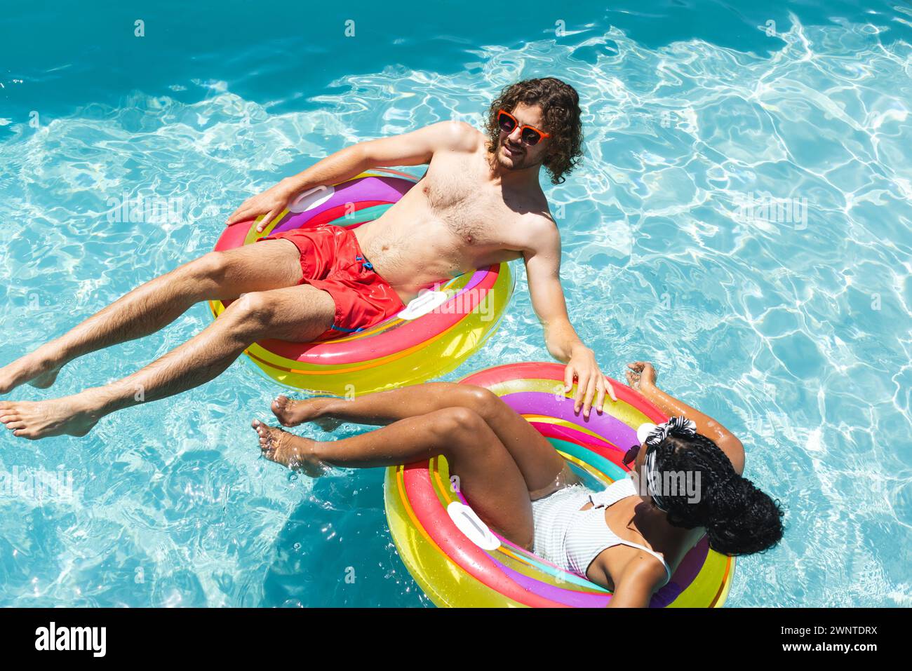 Kaukasischer Mann und afroamerikanische Frau entspannen sich auf farbenfrohen Schwimmbecken Stockfoto