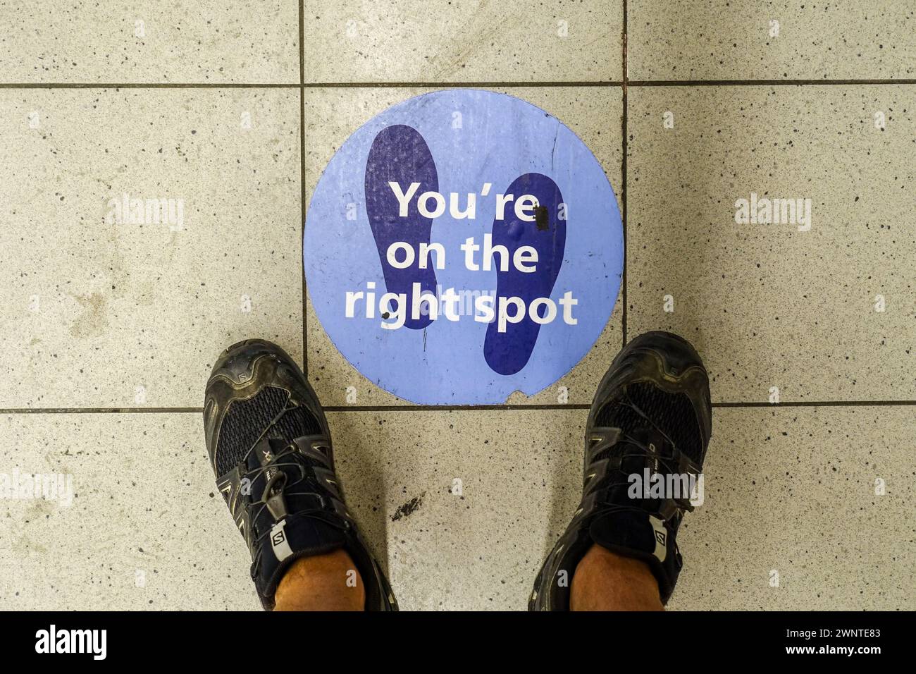 Fuß über der Flughafenetage von Schiphol, mit einem Schild „You're on the right Spot“, während covid-Sperrbeschränkungen für soziale Distanz Stockfoto