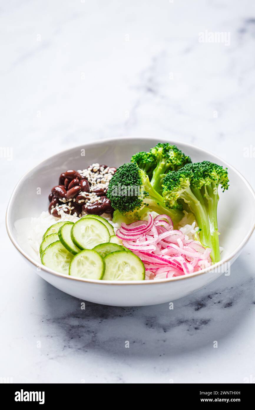 Vegane Poke Schüssel mit Reis, Brokkoli, Gurke, Bohnen und eingelegten roten Zwiebeln, Hintergrund aus weißem Marmor. Stockfoto