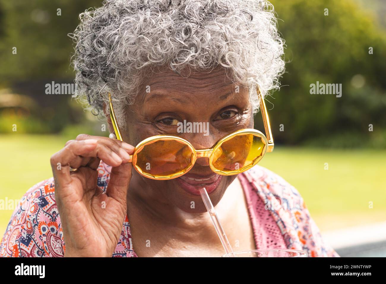 Ältere Frau mit lockigen grauen Haaren senkt ihre übergroße gelbe Sonnenbrille Stockfoto