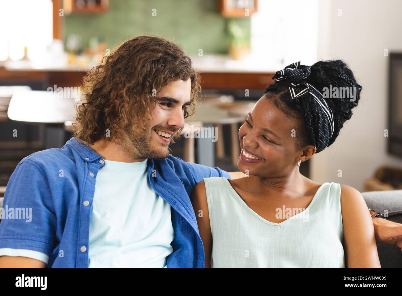 Ein vielseitiges Paar, eine junge Afroamerikanerin und ein kaukasischer Mann teilen sich einen freudigen Moment auf der Couch Stockfoto