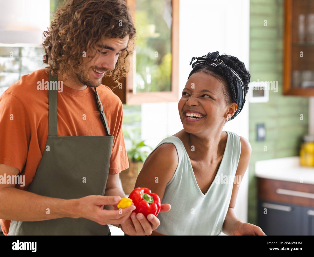 Ein vielseitiges Paar, eine junge Afroamerikanerin und ein kaukasischer Mann lachen in einer Küche Stockfoto