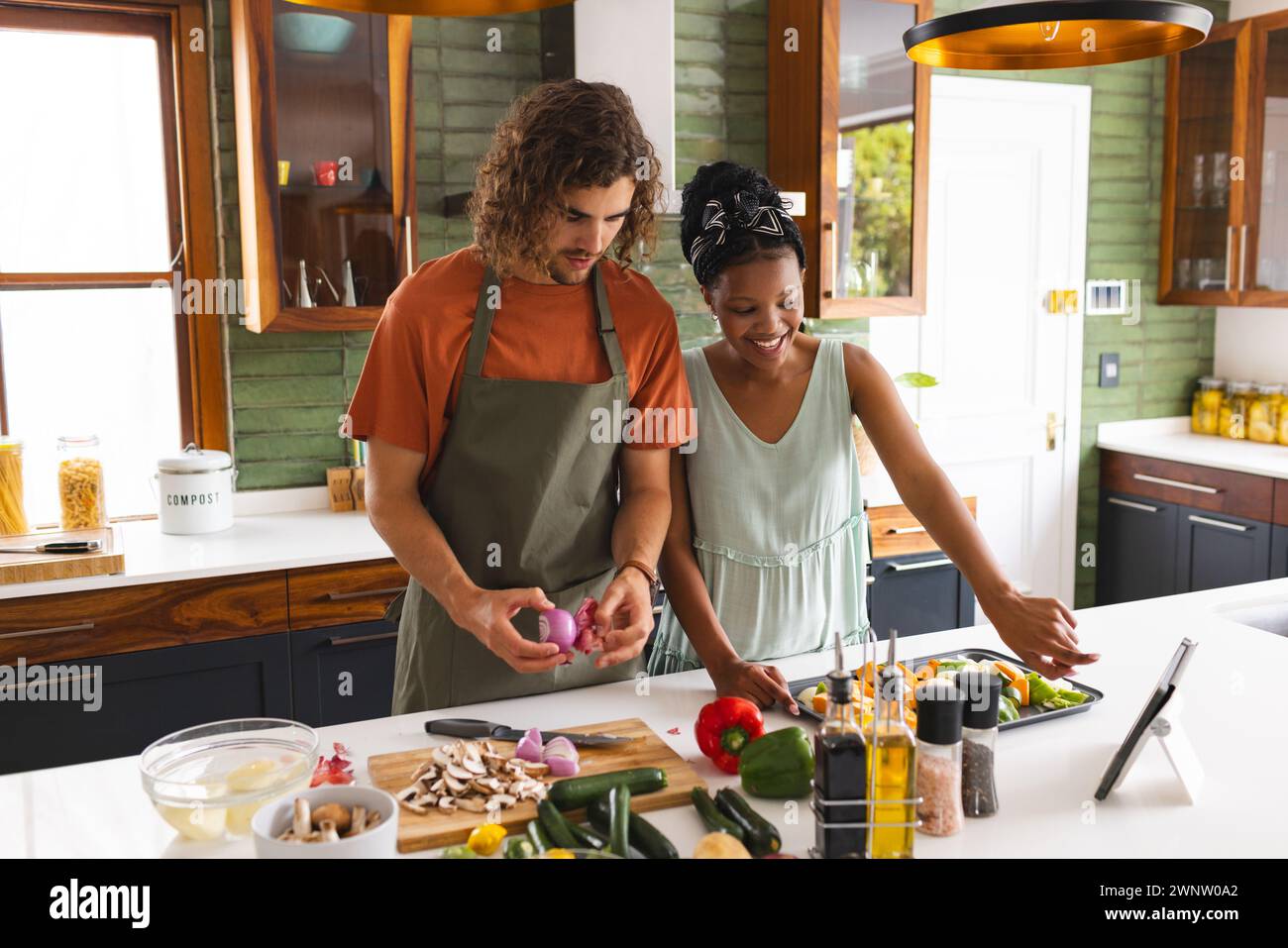 Ein vielseitiges Paar, eine junge Afroamerikanerin und ein kaukasischer Mann kochen zusammen in einer sonnigen Küche Stockfoto