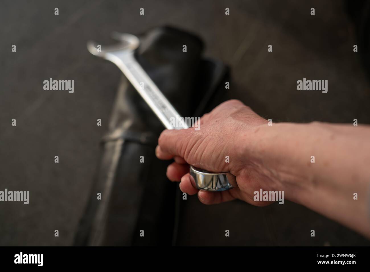Arm, der einen großen Schraubenschlüssel hält, Schlüsselsack auf dem Tisch liegt. Schwenken Sie einen Schraubenschlüssel in diagonaler Position, geringe Schärfentiefe, nur handscharf, Ende des Werkzeugs unscharf. Stockfoto