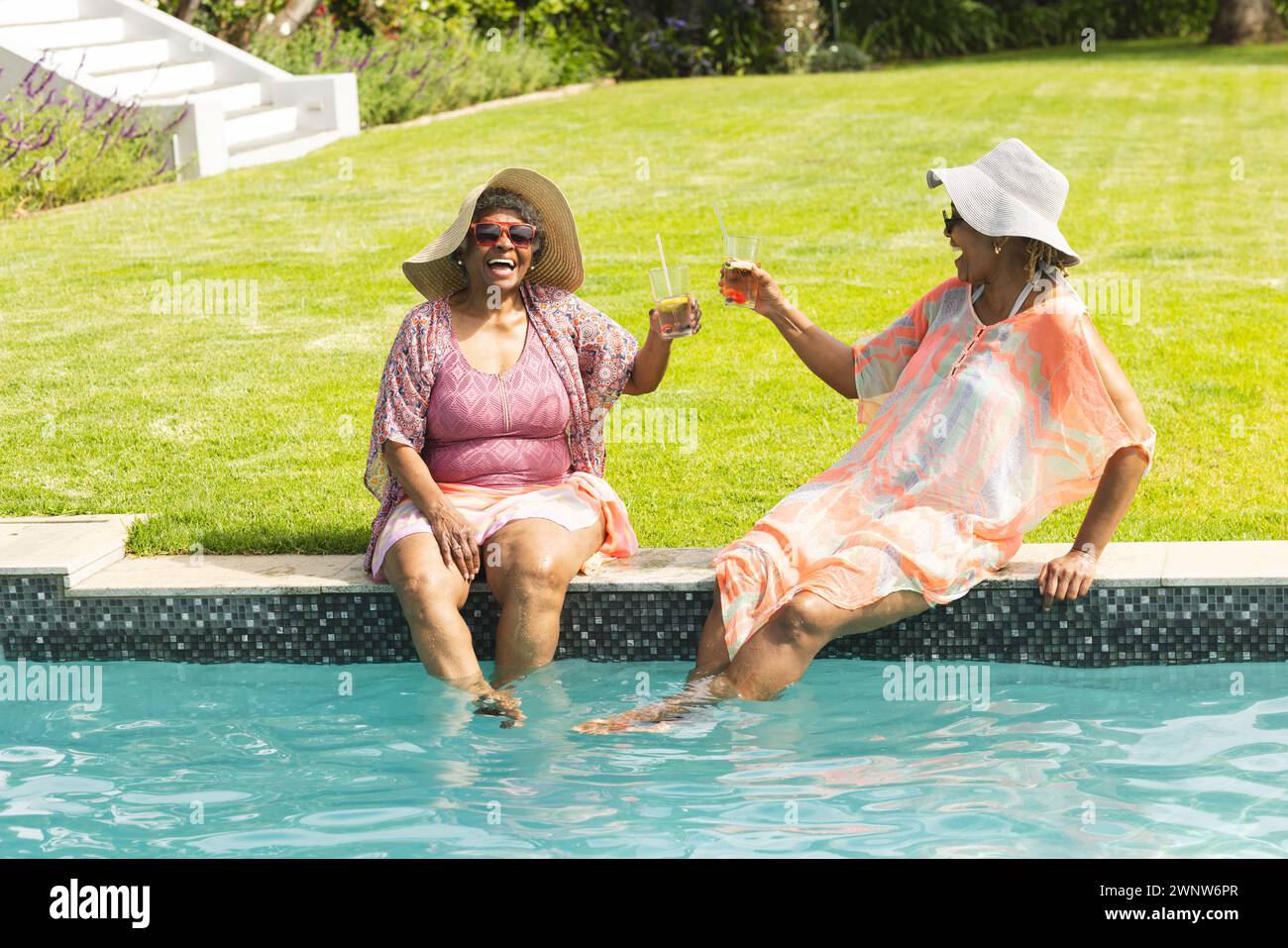 Eine ältere afroamerikanische Frau lacht mit einem Freund am Pool, der beide Getränke hält Stockfoto