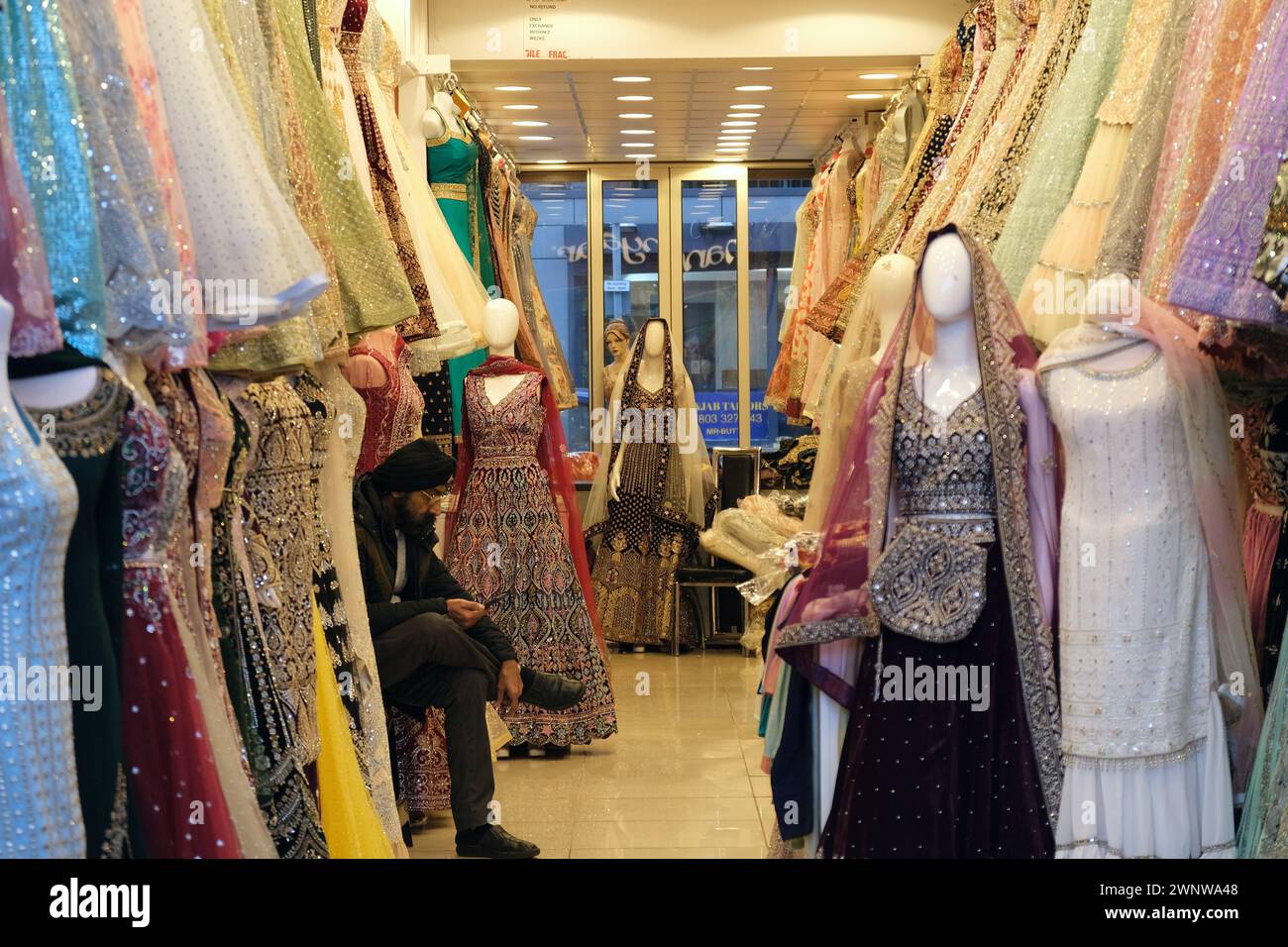 Ein Mann sitzt in seinem Kleiderladen und verkauft südasiatische Kleider in Southall, West London Stockfoto