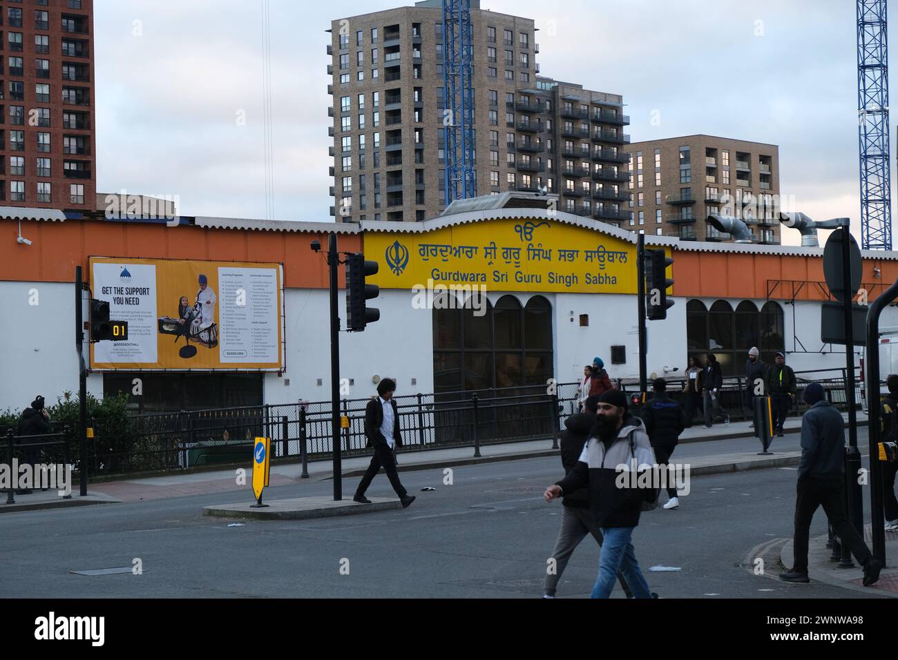 Männer überqueren die Straße vor einem großen Sikh Gurdwara in Southall, einem Gebiet im Westen Londons mit einer großen ethnischen Sikh-Bevölkerung Stockfoto