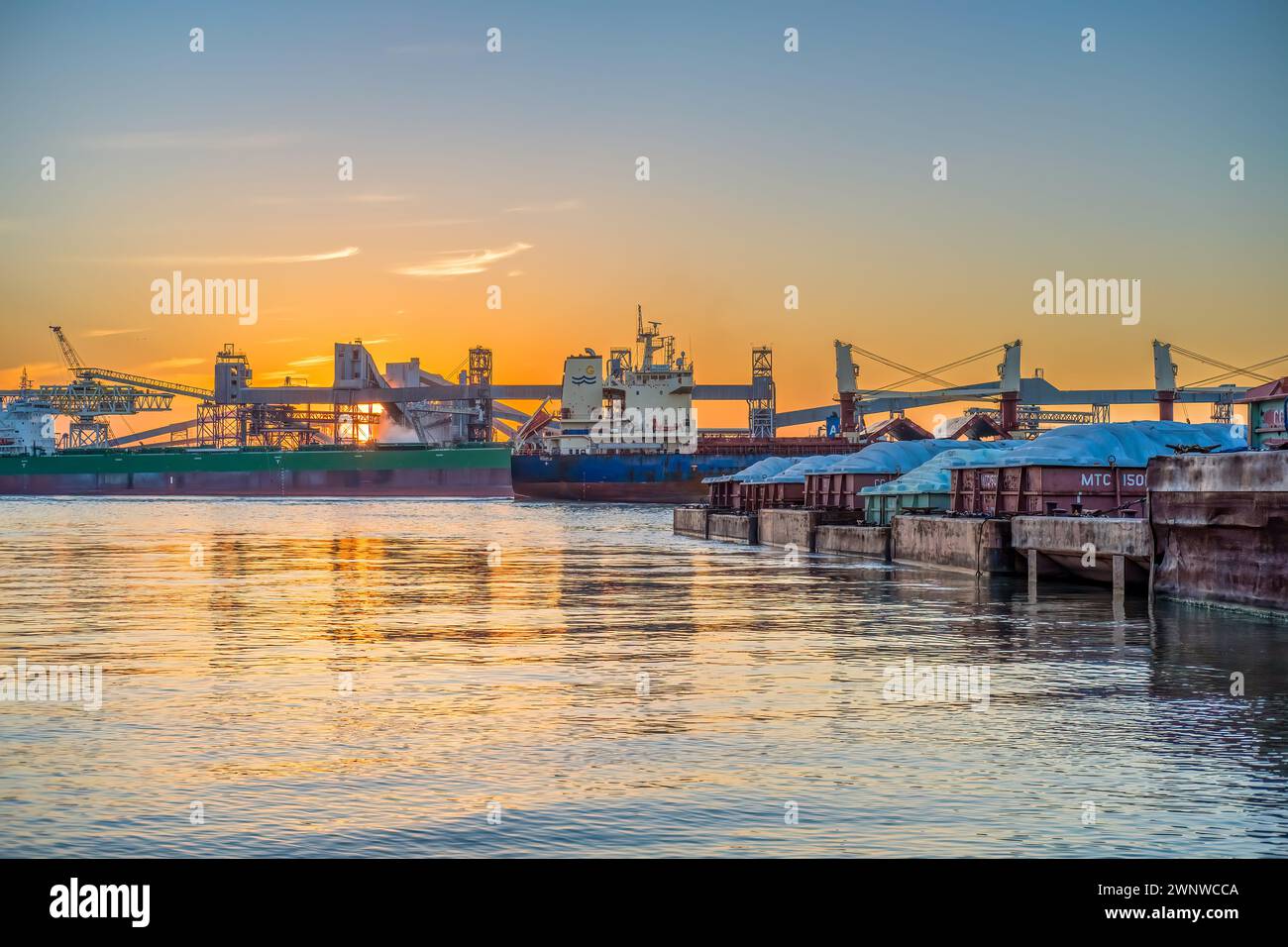 NEW ORLEANS, LA, USA – 14. OKTOBER 2020: Szene am Mississippi-Fluss bei Sonnenuntergang mit Frachtschiffen, Lastkähnen und Getreideaufzügen Stockfoto
